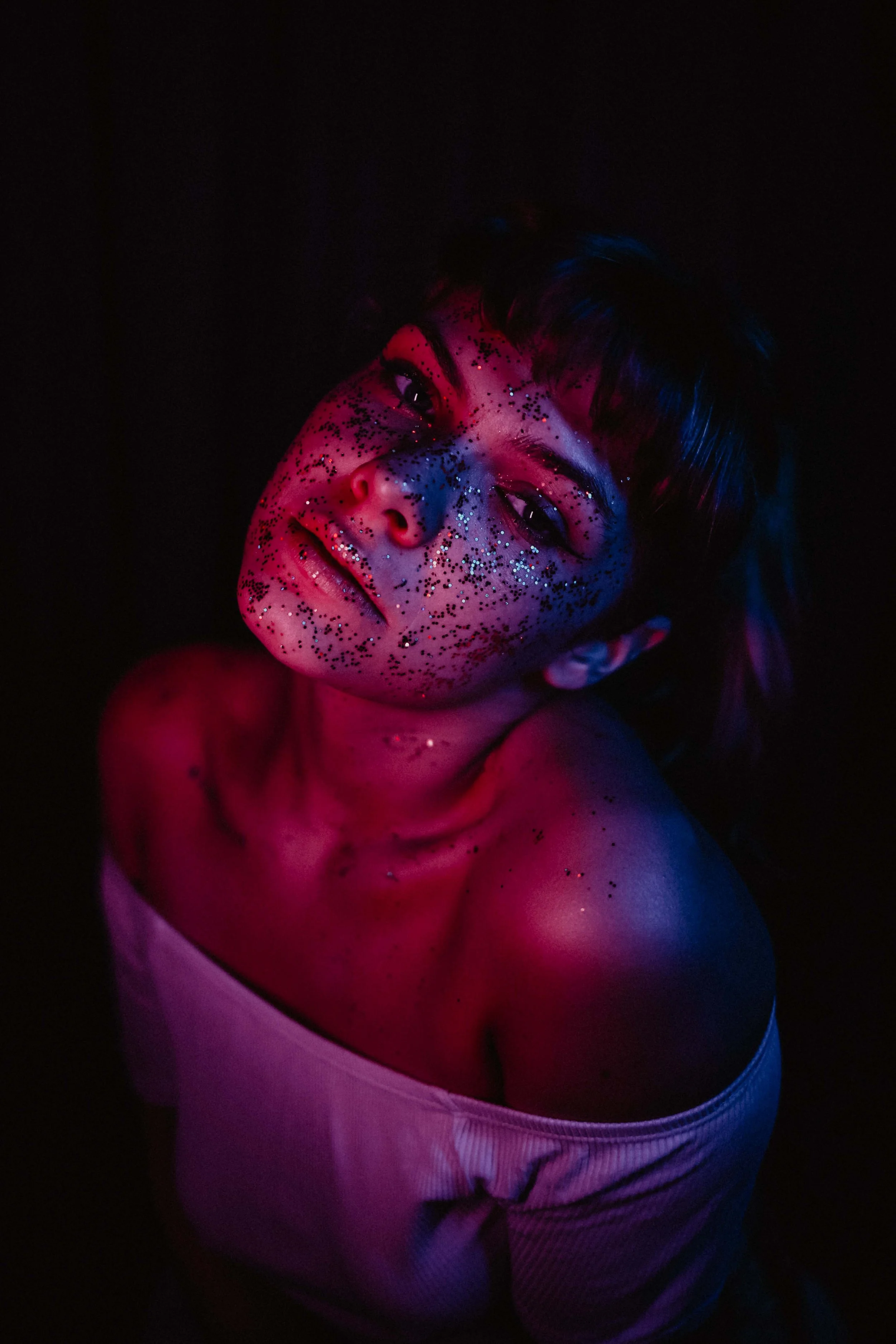 Jeune femme avec maquillage brillant et confettis sous un éclairage coloré sombre.