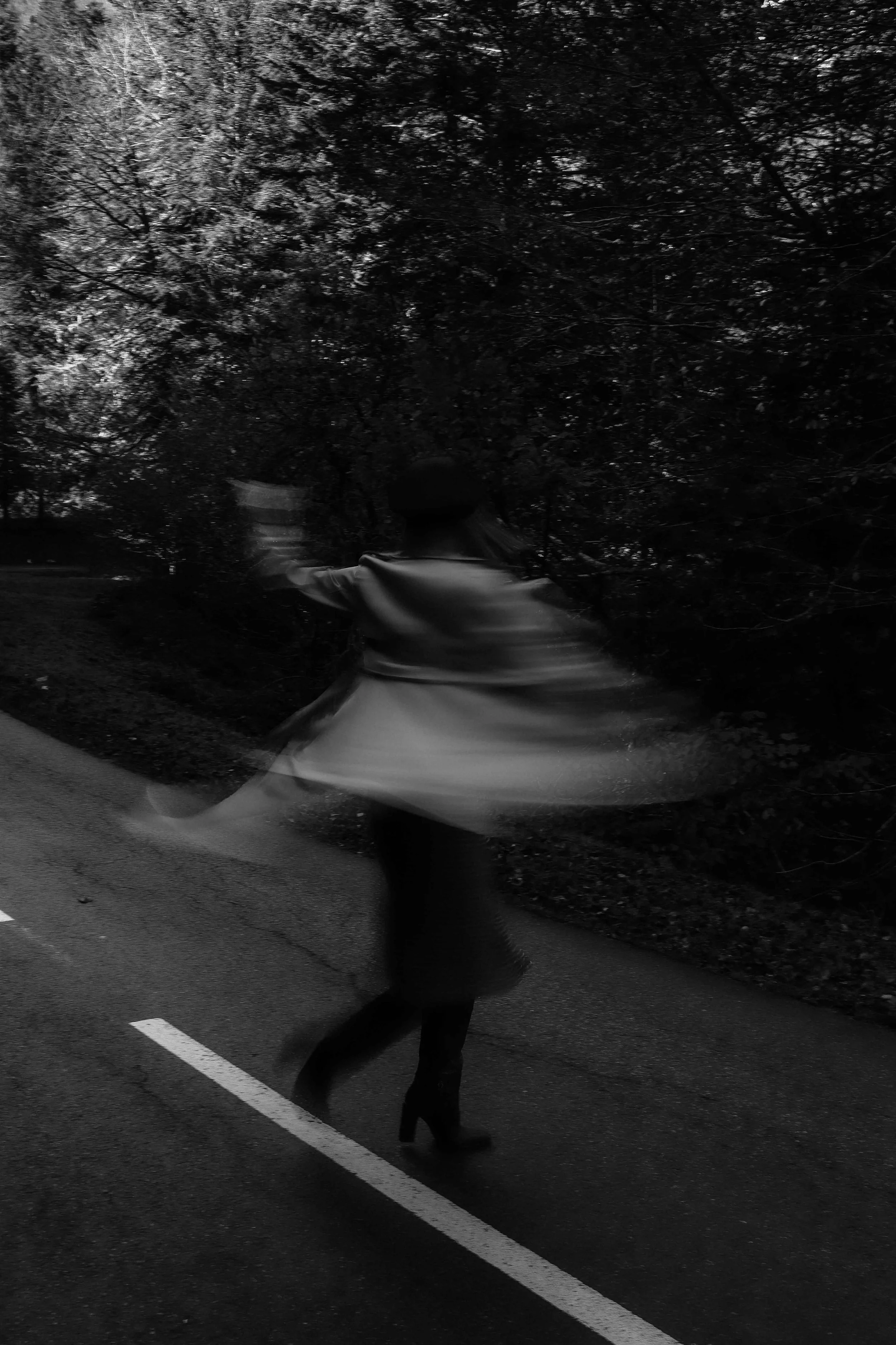 Une personne portant une jupe et des bottes faites face à un arrière-plan d'arbres, marche ou tourne sur une route pavée.