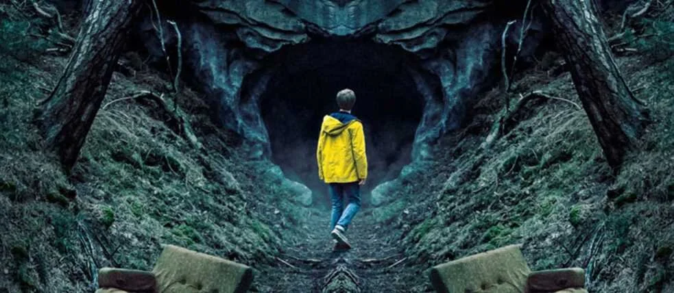 Une personne avec une veste jaune marche dans une grotte ou un tunnel naturel entouré de roche et de végétation, avec deux meubles en avant.