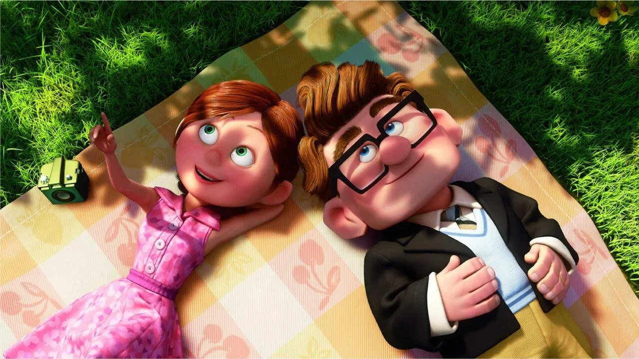 Deux personnages de dessin animé, une fille aux cheveux courts roux en robe rose, et un garçon à cheveux bruns avec lunettes, allongés sur une couverture en tartan, dans un champ d'herbe verte au soleil.