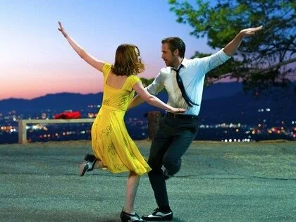 Un couple danse avec un arrière-plan de coucher de soleil et une ville illuminée.