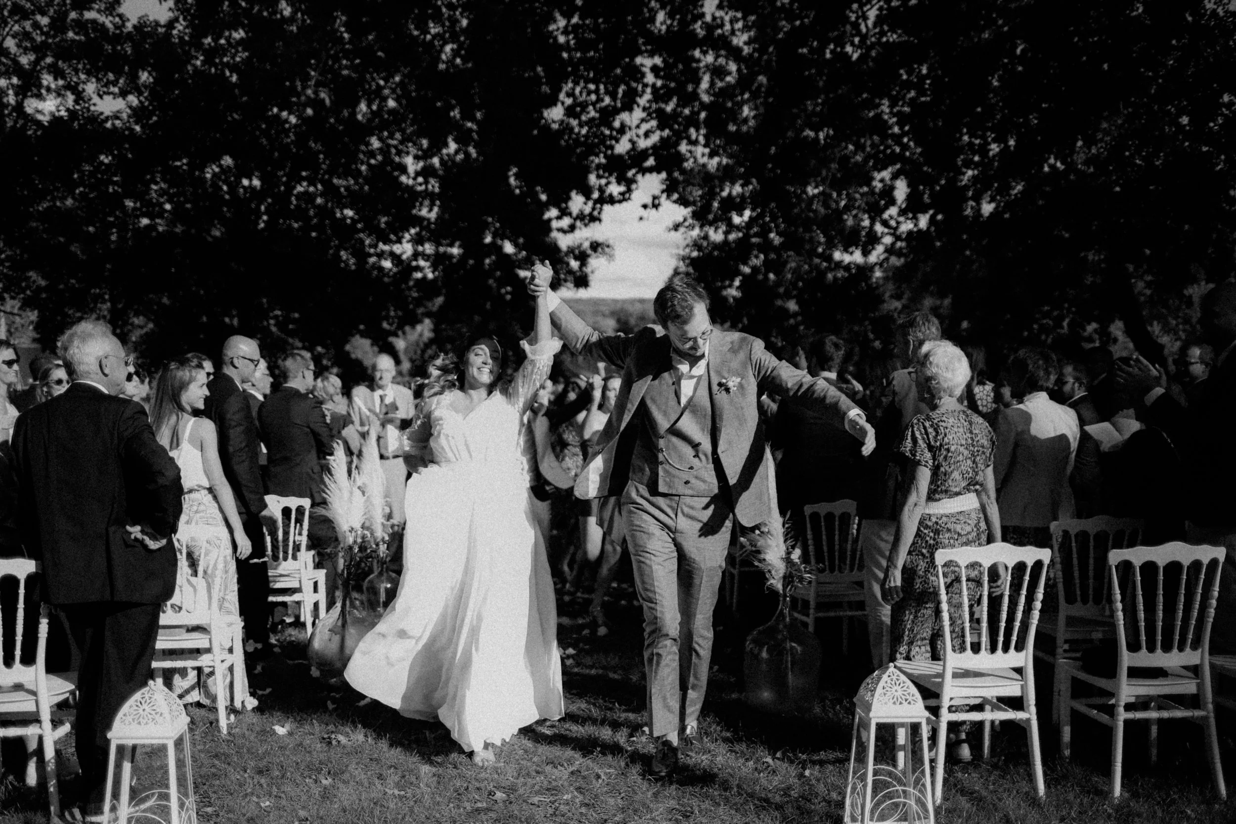 Une mariée et un marié dansant lors d'une réception en plein air, entourés d'invités, avec des chaises et des décorations, sous un ciel clair.