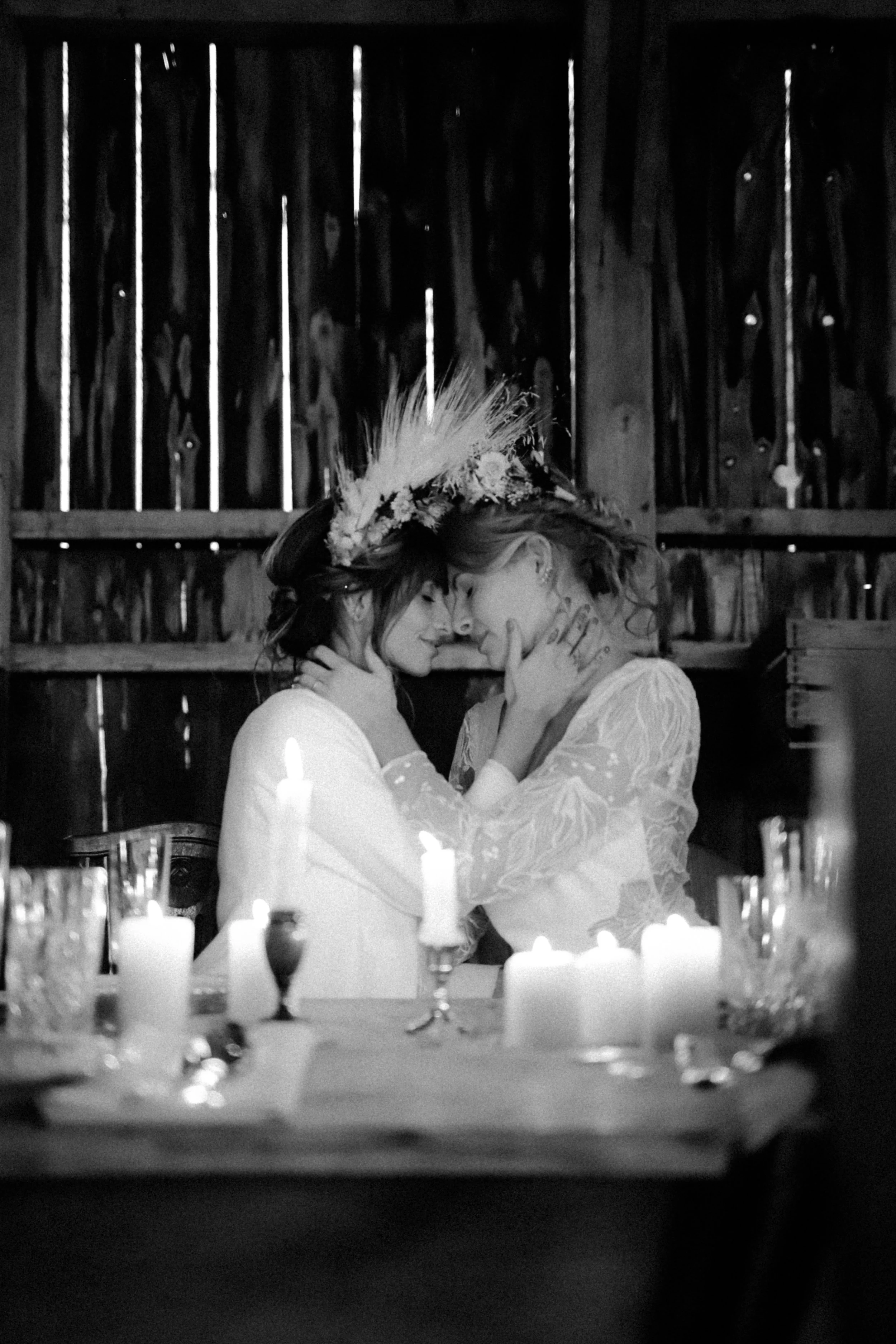 Deux femmes s'embrassent tendrement dans une ambiance romantique, entourées de bougies allumées, avec un fond en bois.
