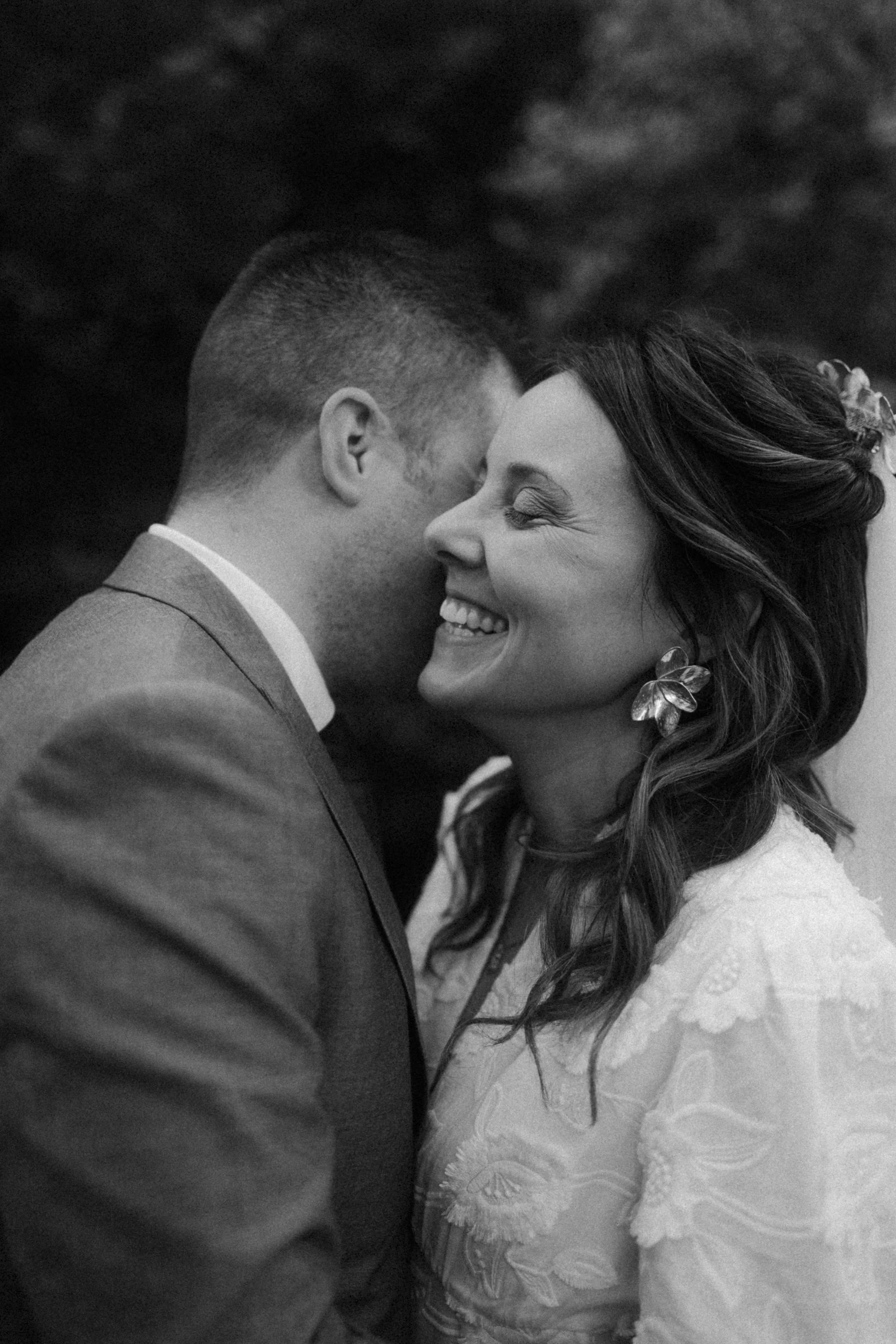 Un couple heureux échangeant un bisou intime lors d'un mariage, en noir et blanc.