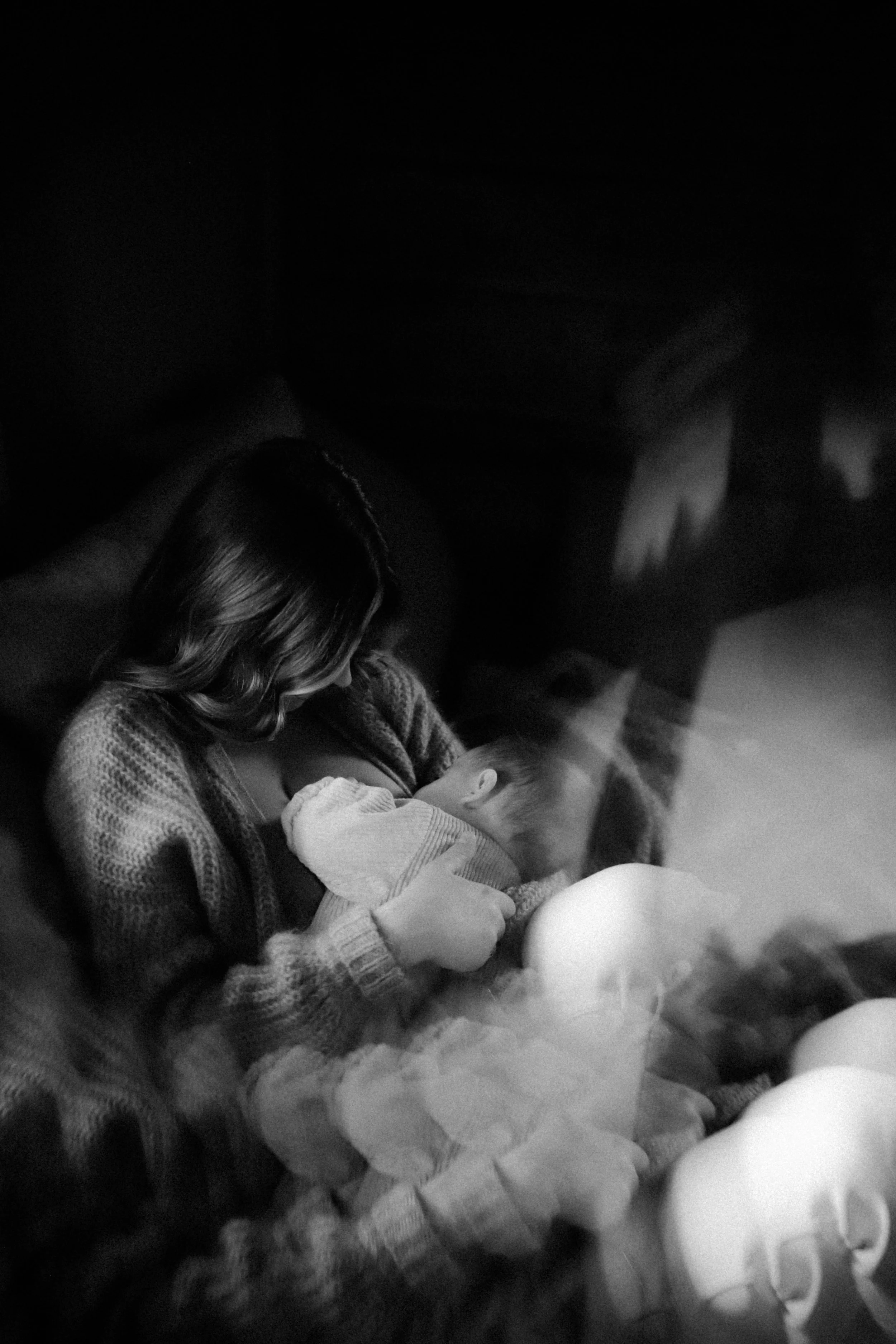 Une femme tient un bébé dans ses bras dans un environnement sombre, avec une ambiance douce et intime.