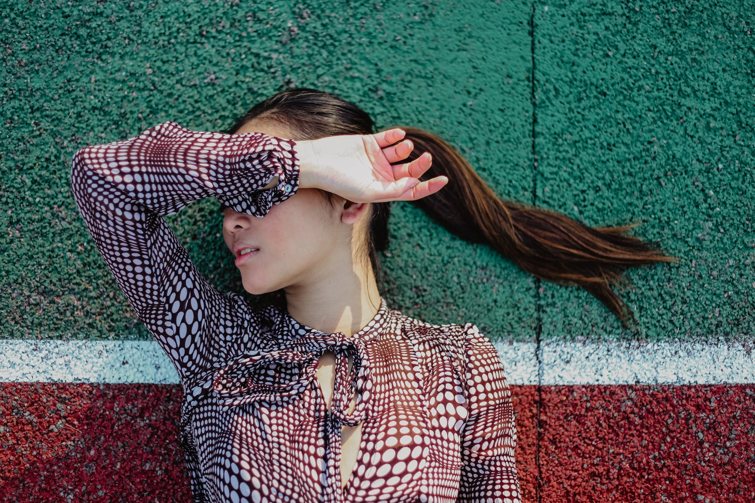 Femme allongée sur un sol coloré, couvrant ses yeux avec une main. La surface est divisée en sections de vert, blanc, et rouge.