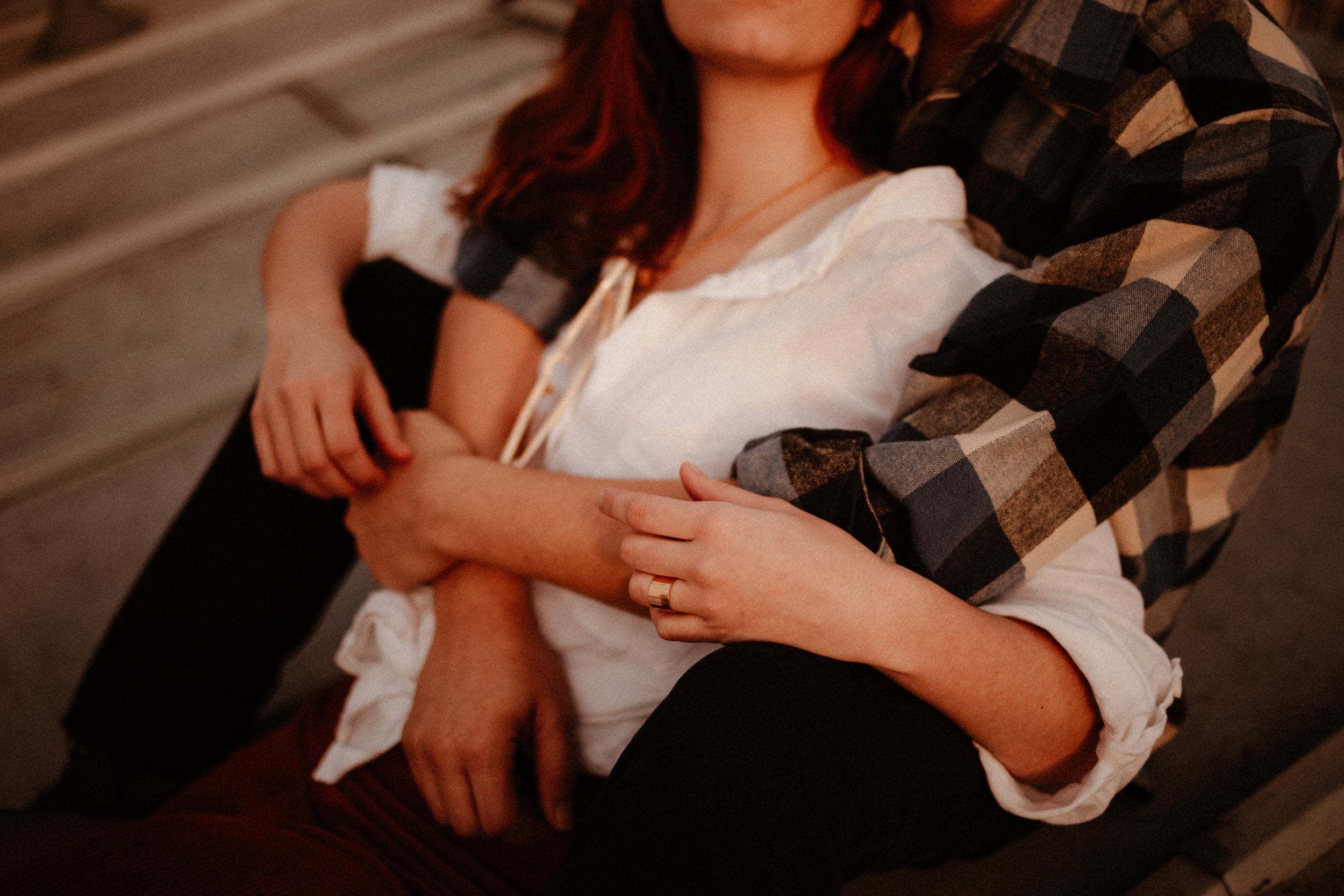 Deux personnes, une femme aux cheveux roux et une autre personne dont on ne voit pas le visage, sont en train de s'étreindre de façon intime. La femme porte une chemise blanche avec les manches retroussées et un anneau à la main, l'autre personne por