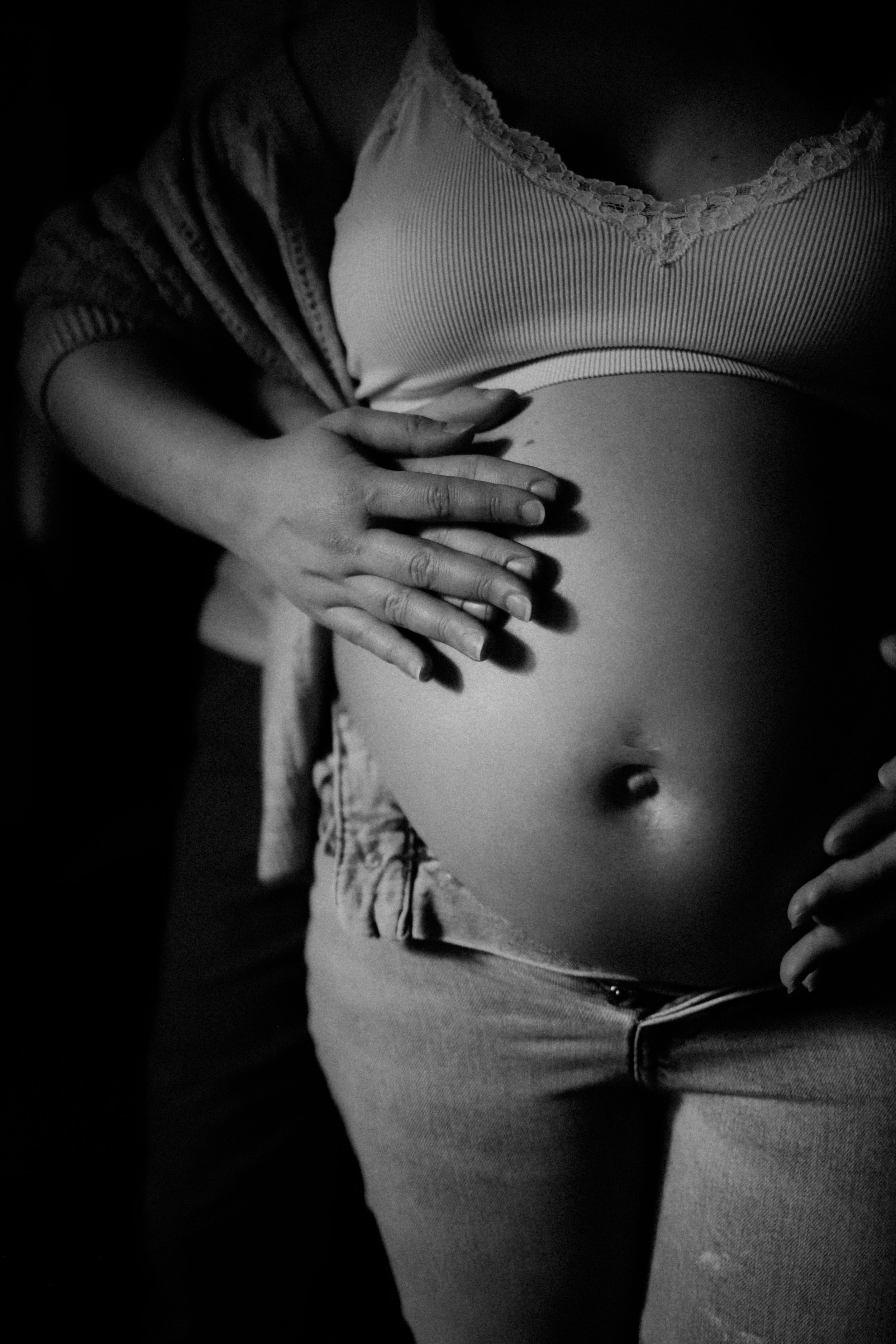 Une femme enceinte portant un haut sans manches et un pantalon, avec ses mains posées sur son ventre dans une photo en noir et blanc.