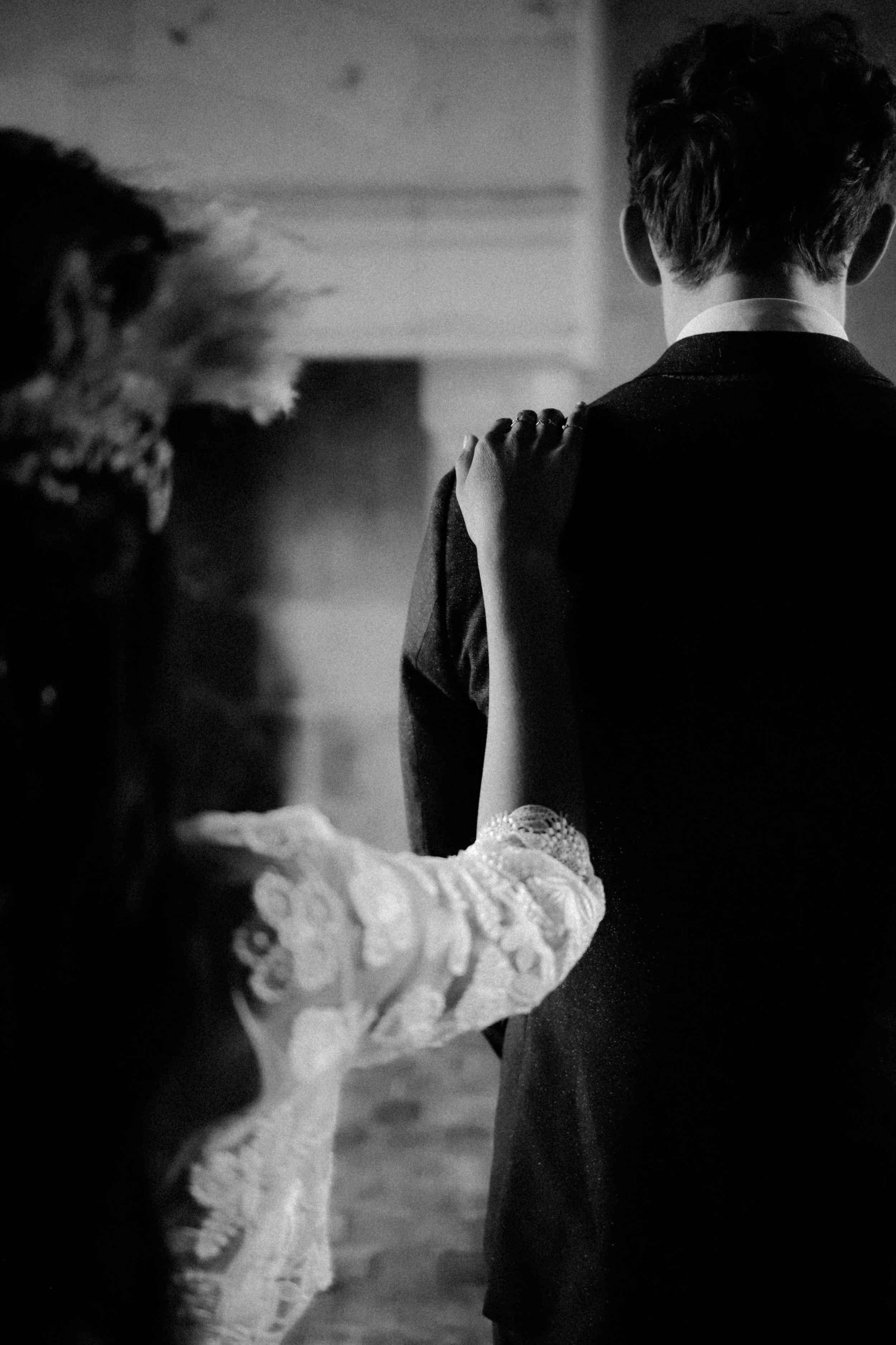 Un couple dancing, vue de dos, en noir et blanc, avec une femme en robe délicate de dentelle, tenant le bras d'un homme en costume.