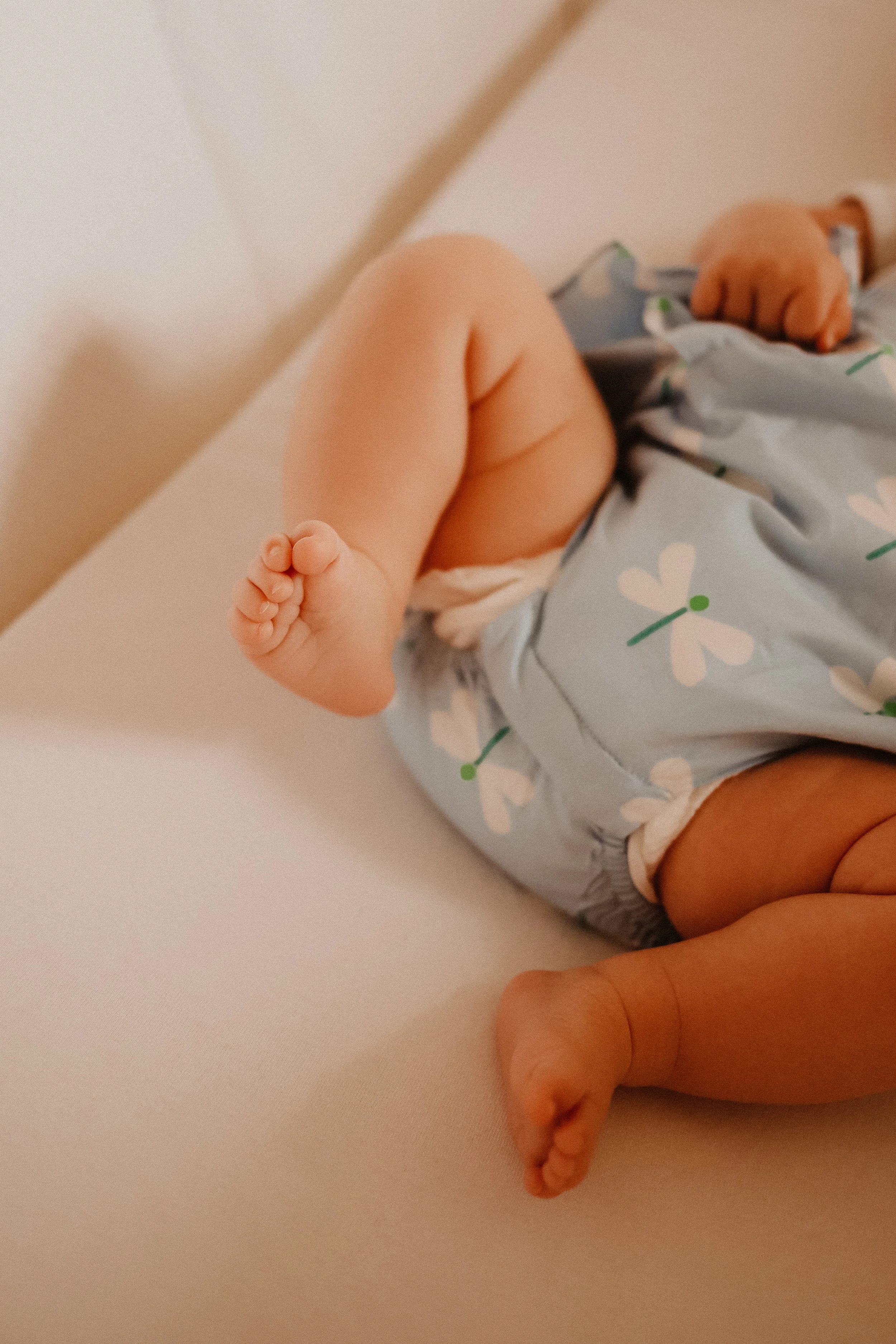 Un bébé allongé sur un lit, portant une couche et un pyjama bleu avec des motifs de papillons blancs et verts.