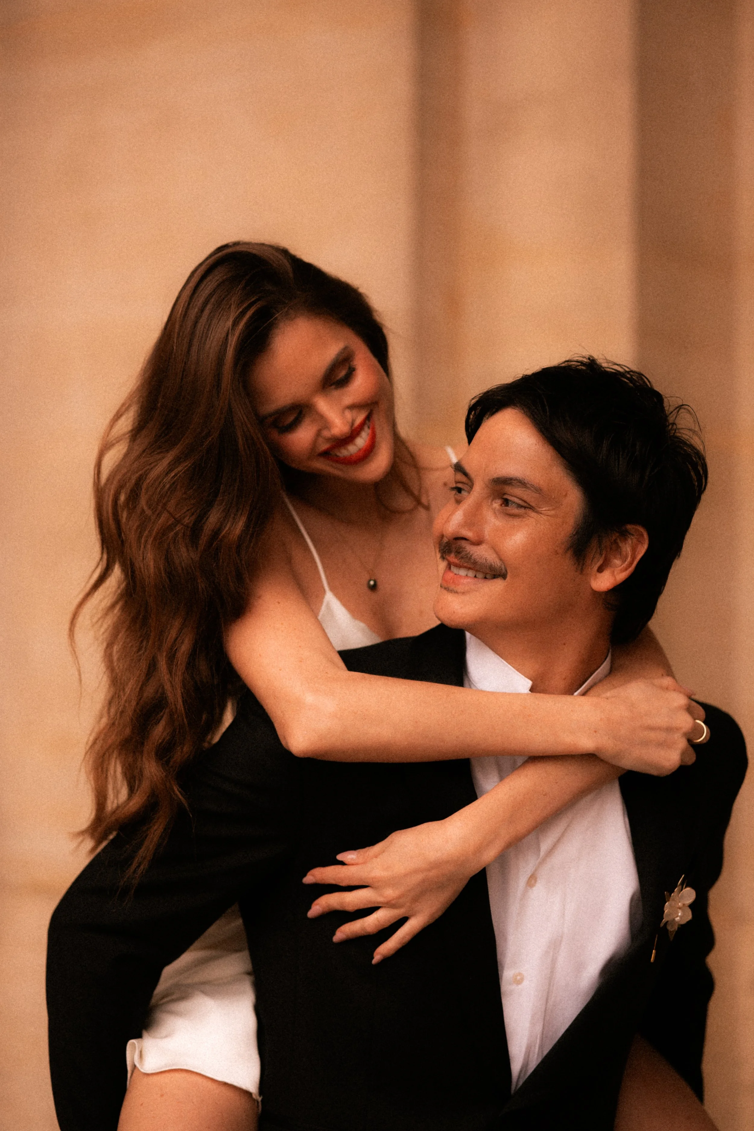 Un couple souriant, l'homme portant un costume noir et une femme en robe blanche, partageant un moment romantique