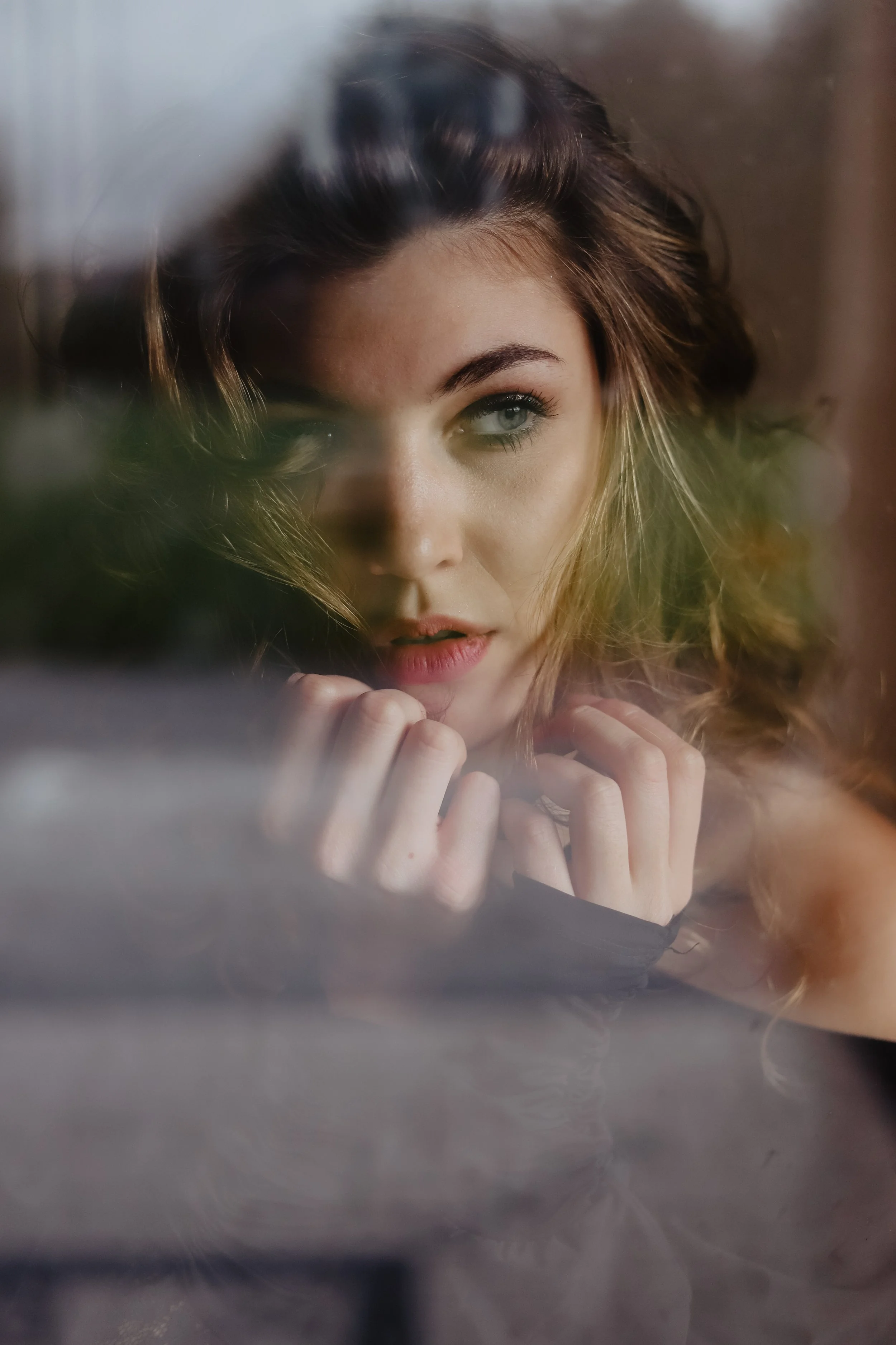 Jeune femme regarde à travers une fenêtre, avec un focus sur son visage et ses yeux.