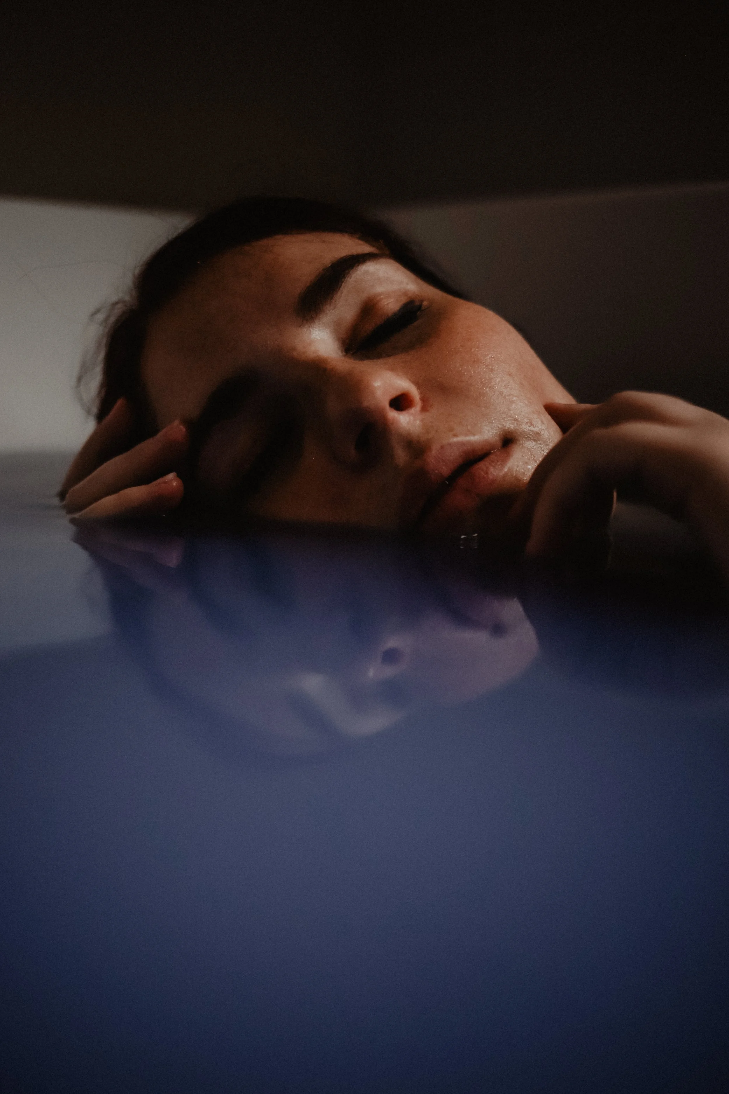 Une personne repose sa tête sur une surface, le visage partiellement immergé dans l'eau, avec une expression de calme.