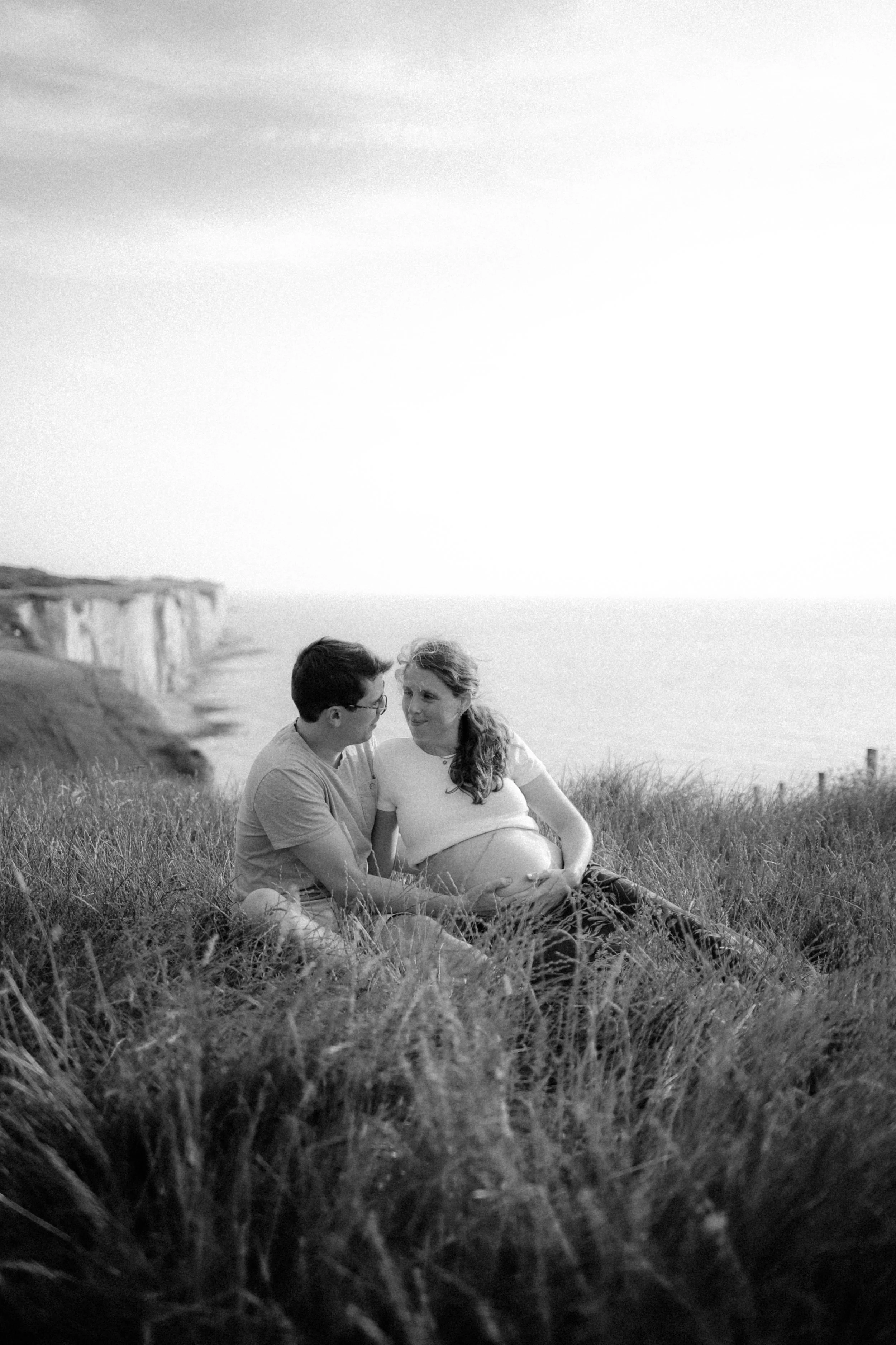 Un couple assis dans l'herbe près des falaises au bord de la mer, en noir et blanc