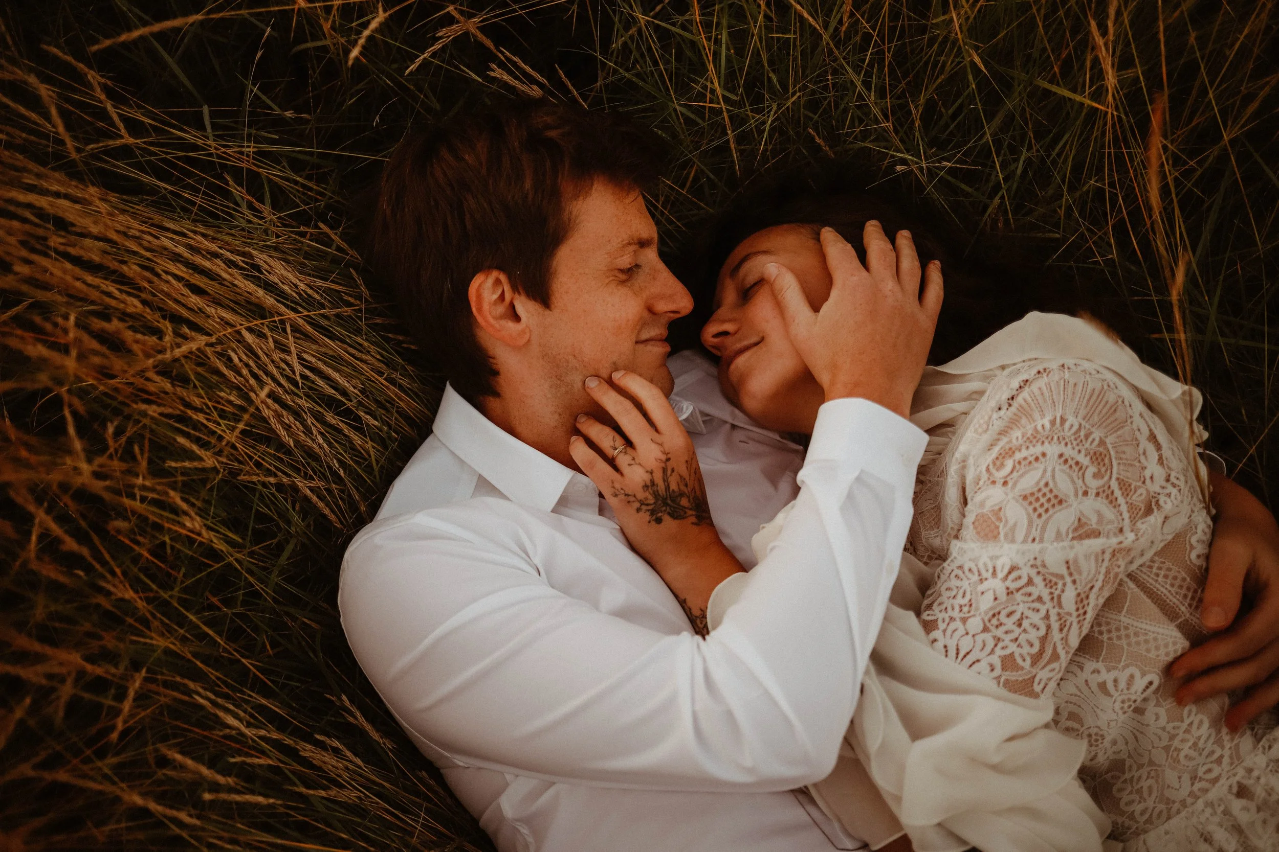 Un couple allongé dans de l'herbe, se regardant tendrement, dans un cadre naturel, ambiance intime et douce.