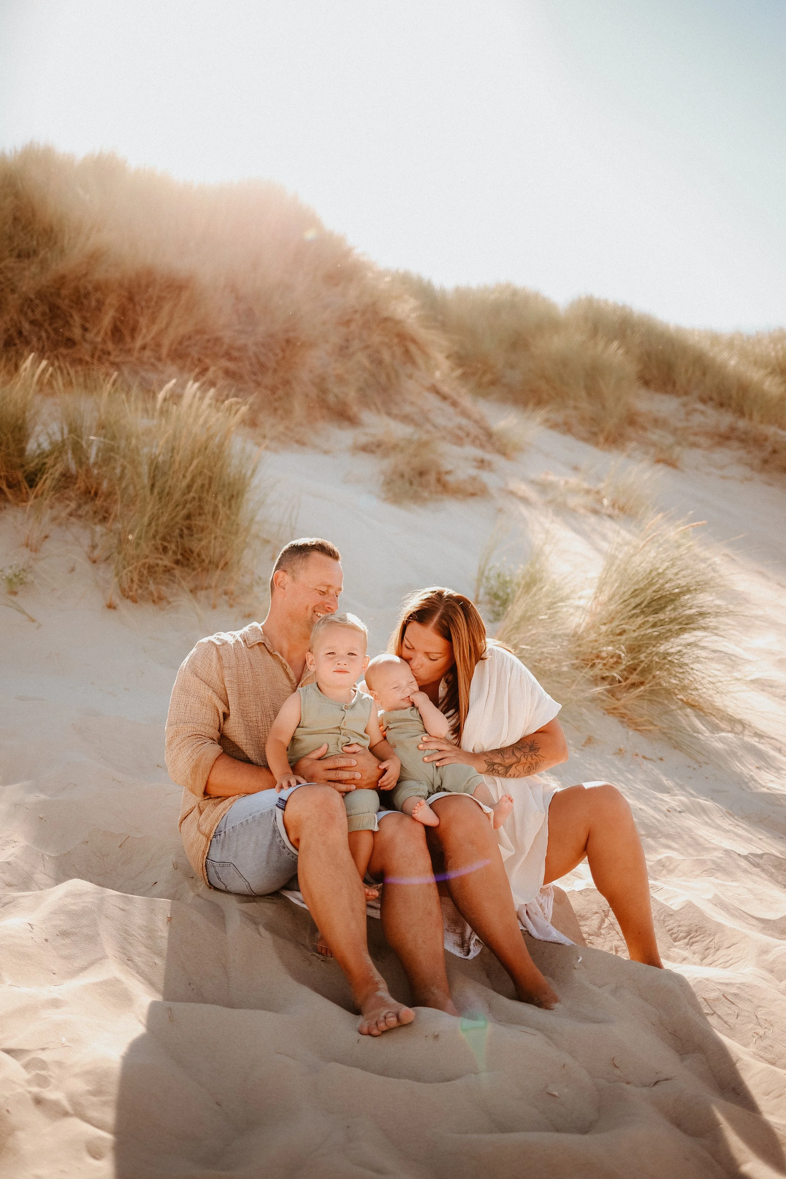 Une famille de quatre personnes assise sur le sable dans un désert de dunes, partageant un moment de tendresse et de complicité.