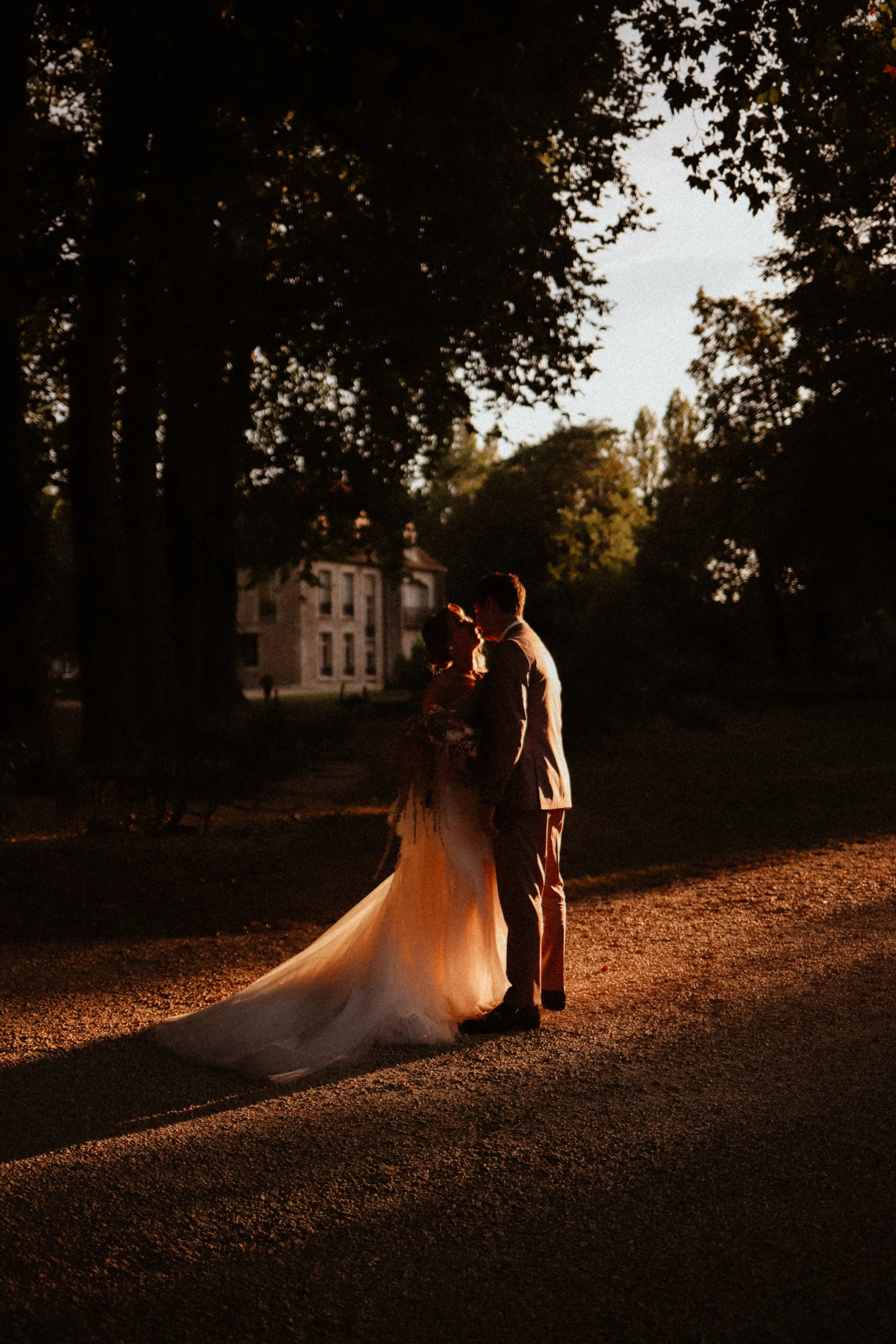 Un couple de mariés silhouette partage un moment romantique lors du coucher de soleil dans un parc.