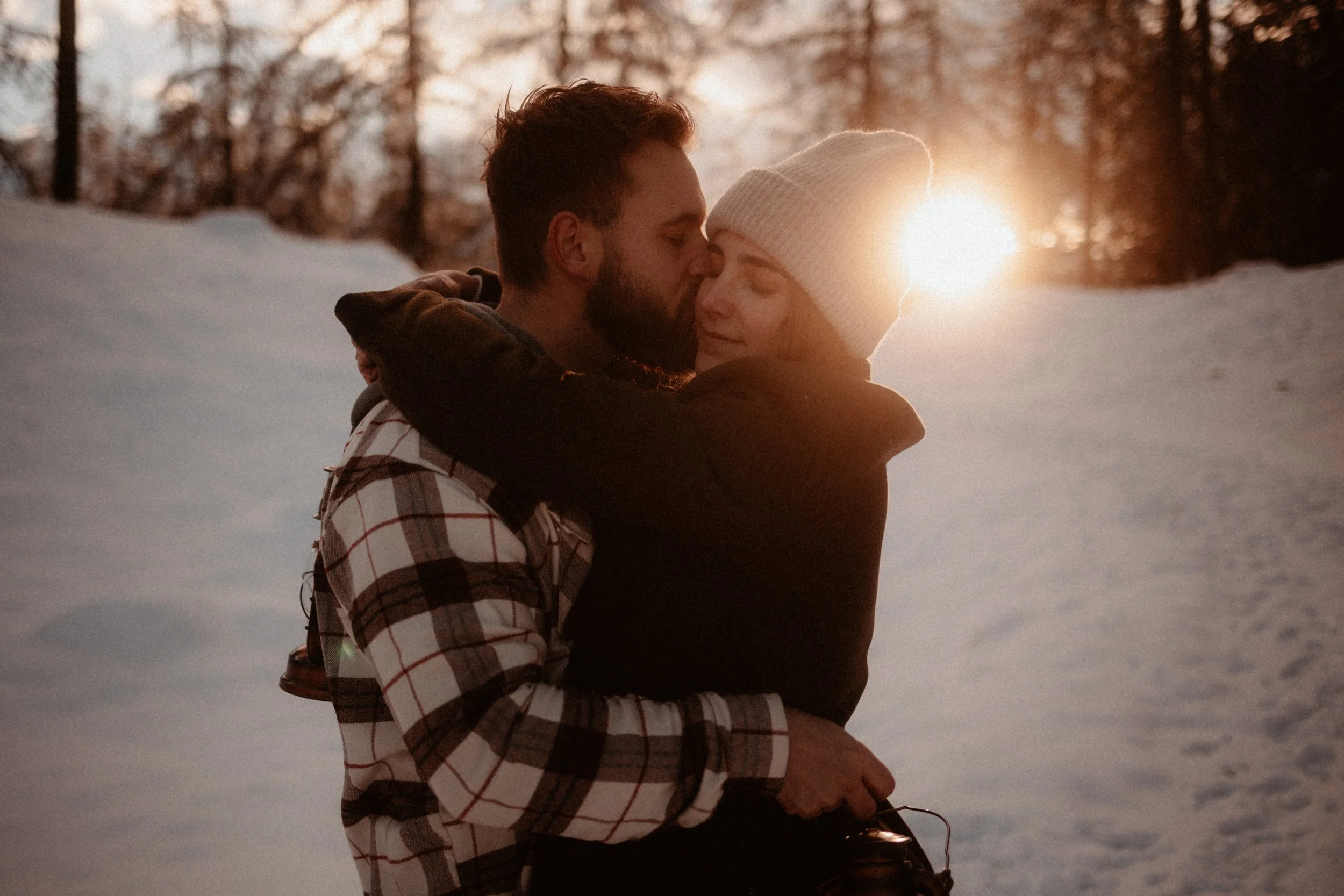 Un couple se serre dans la neige lors d'un coucher de soleil, exprimant de l'amour et de l'affection.
