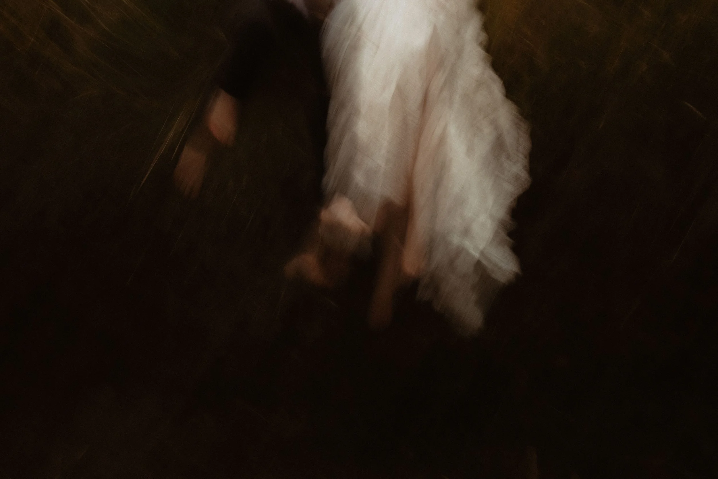 Une personne en robe blanche avec des chaussures plates, vue de dos, marchant sur un sol sombre en bois.