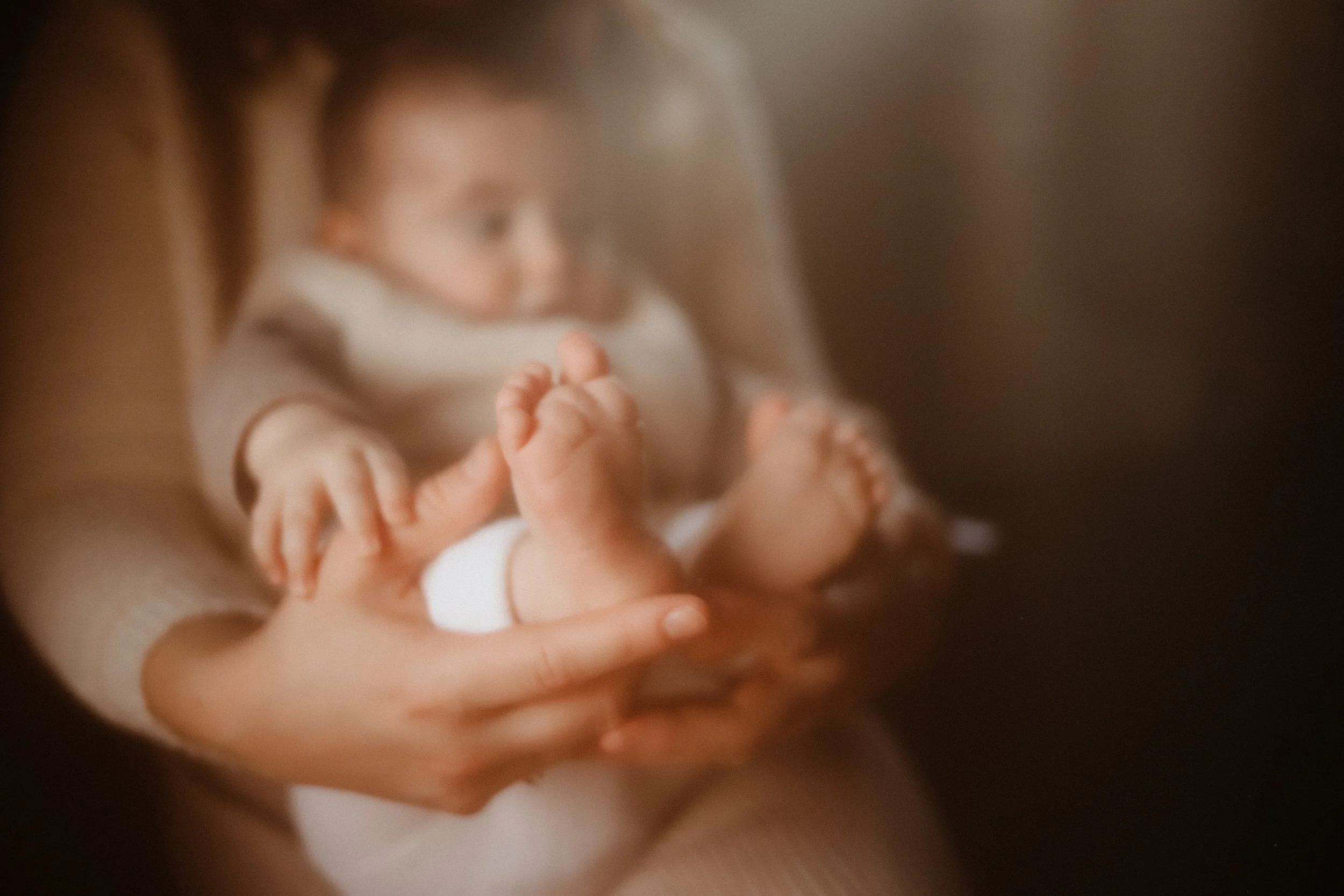 Un bébé tenu dans les bras d'un adulte, avec un focus sur ses petits pieds et ses mains, dans une ambiance chaleureuse.