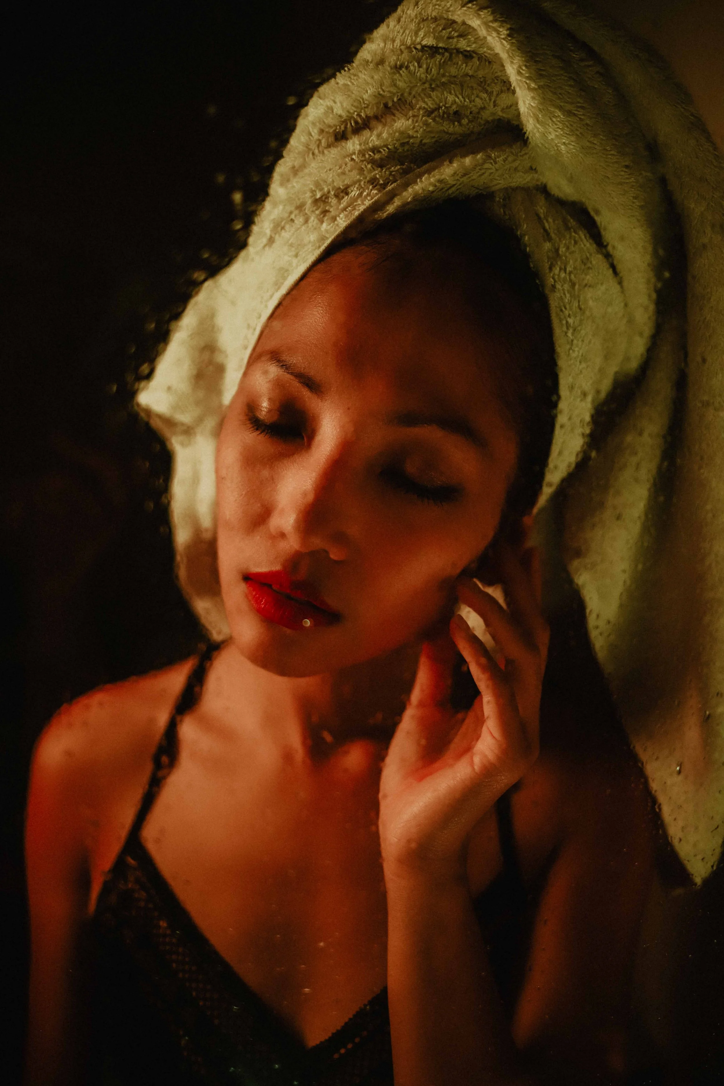 Une femme avec un towel sur la tête, les yeux fermés et portant du maquillage rouge, en train de se détendre.