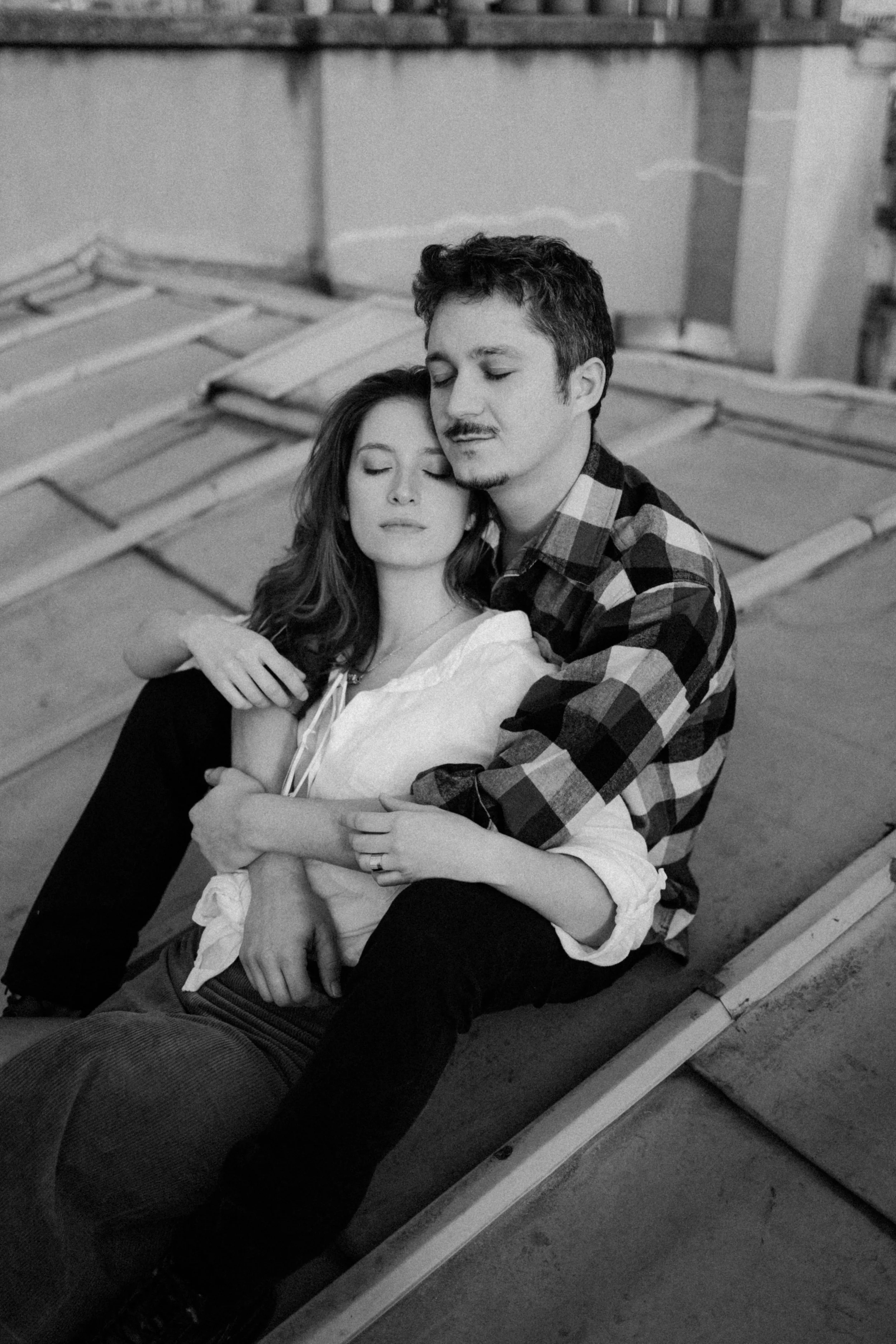 Un jeune couple se tient dans une pose romantique, les yeux fermés, sur une terrasse en toit.