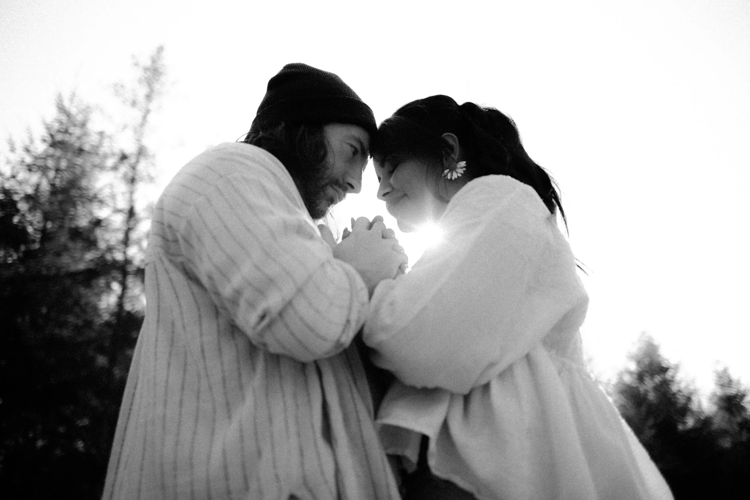 Un couple se tient face à face, main dans la main, avec le soleil en arrière-plan, créant une ambiance intime et romantique.