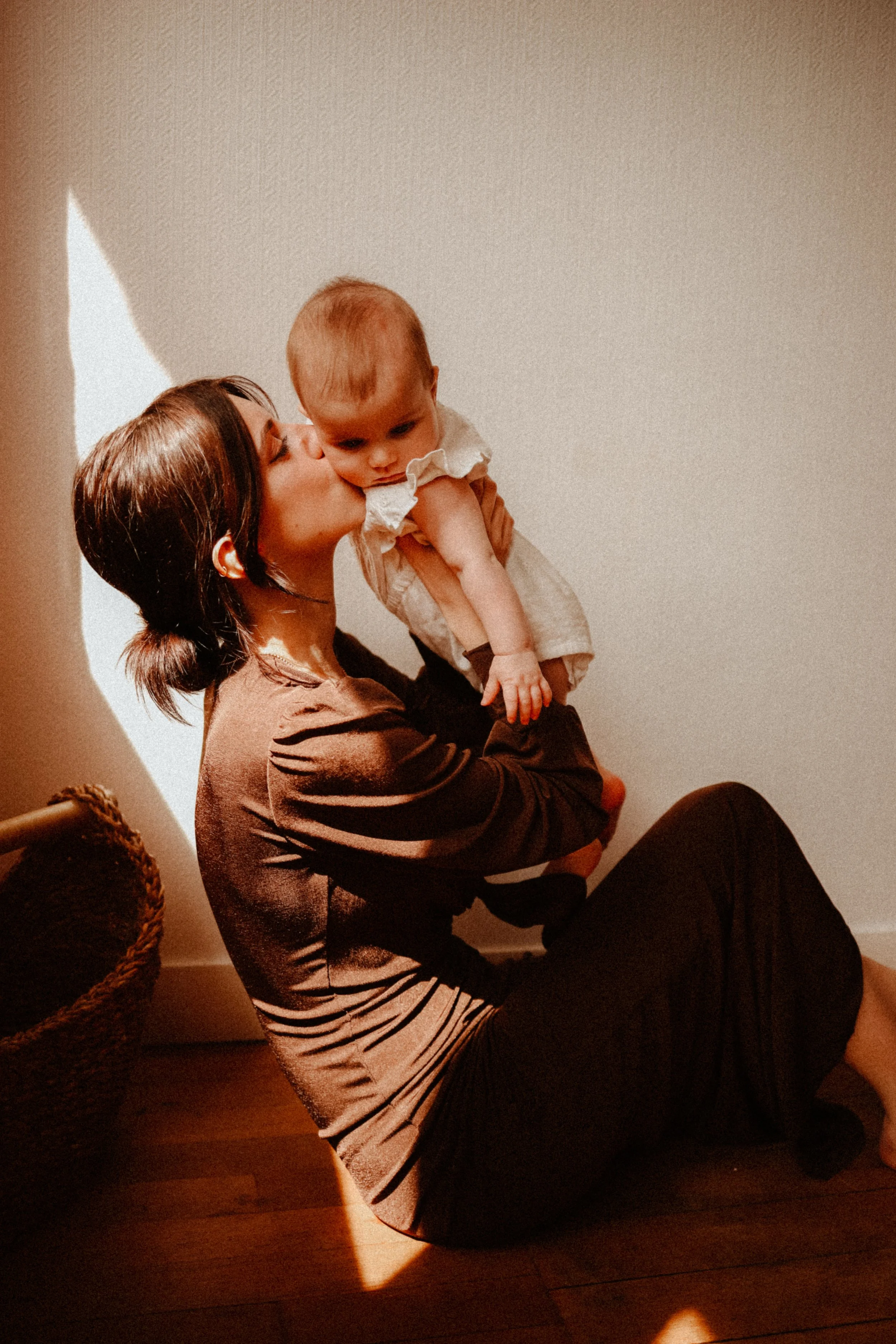 Une femme assise par terre à l'intérieur, embrassant un bébé qu'elle tient dans ses bras.