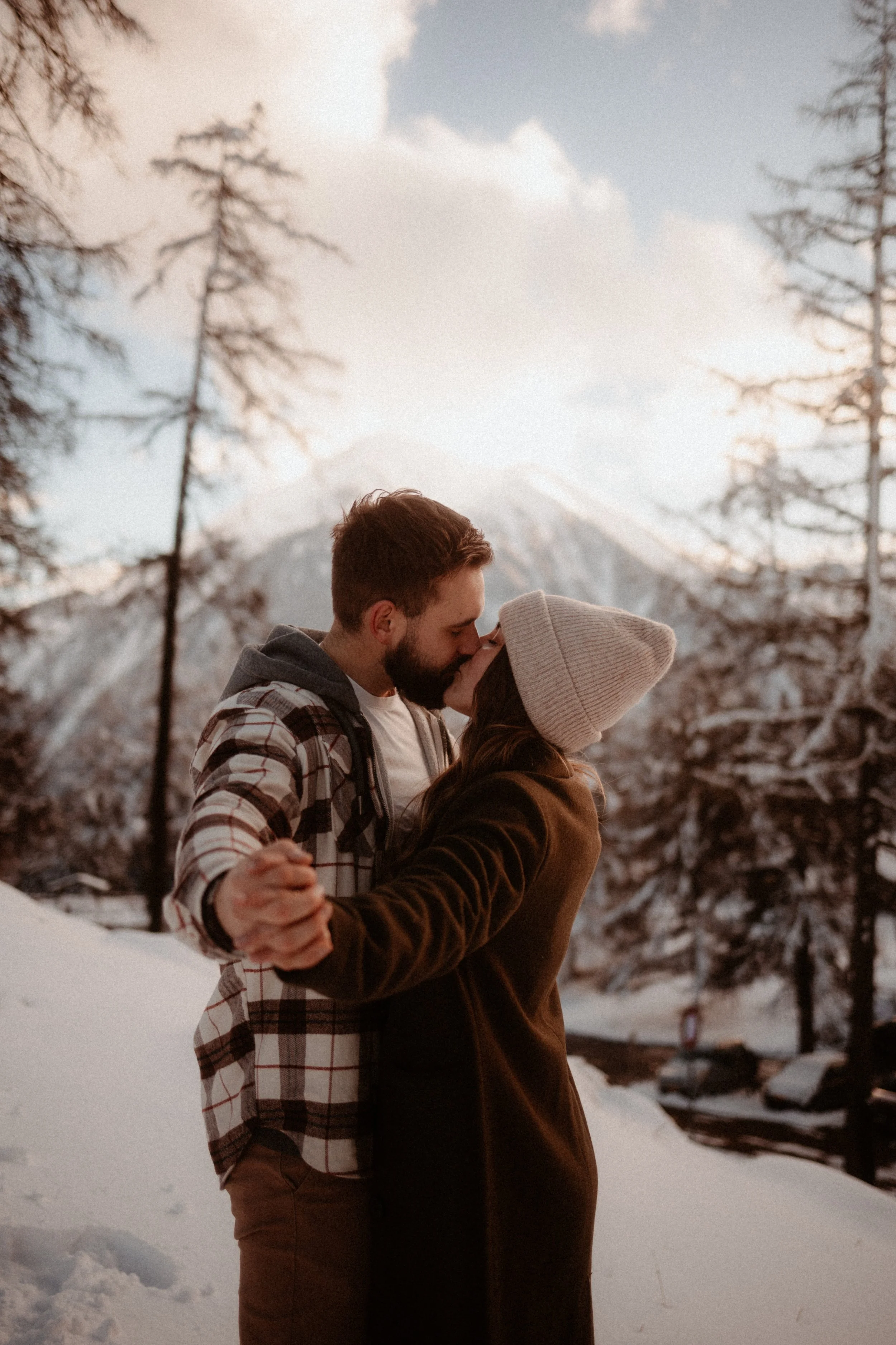 Un couple qui s'embrasse dans la neige en montagne par une journée ensoleillée.
