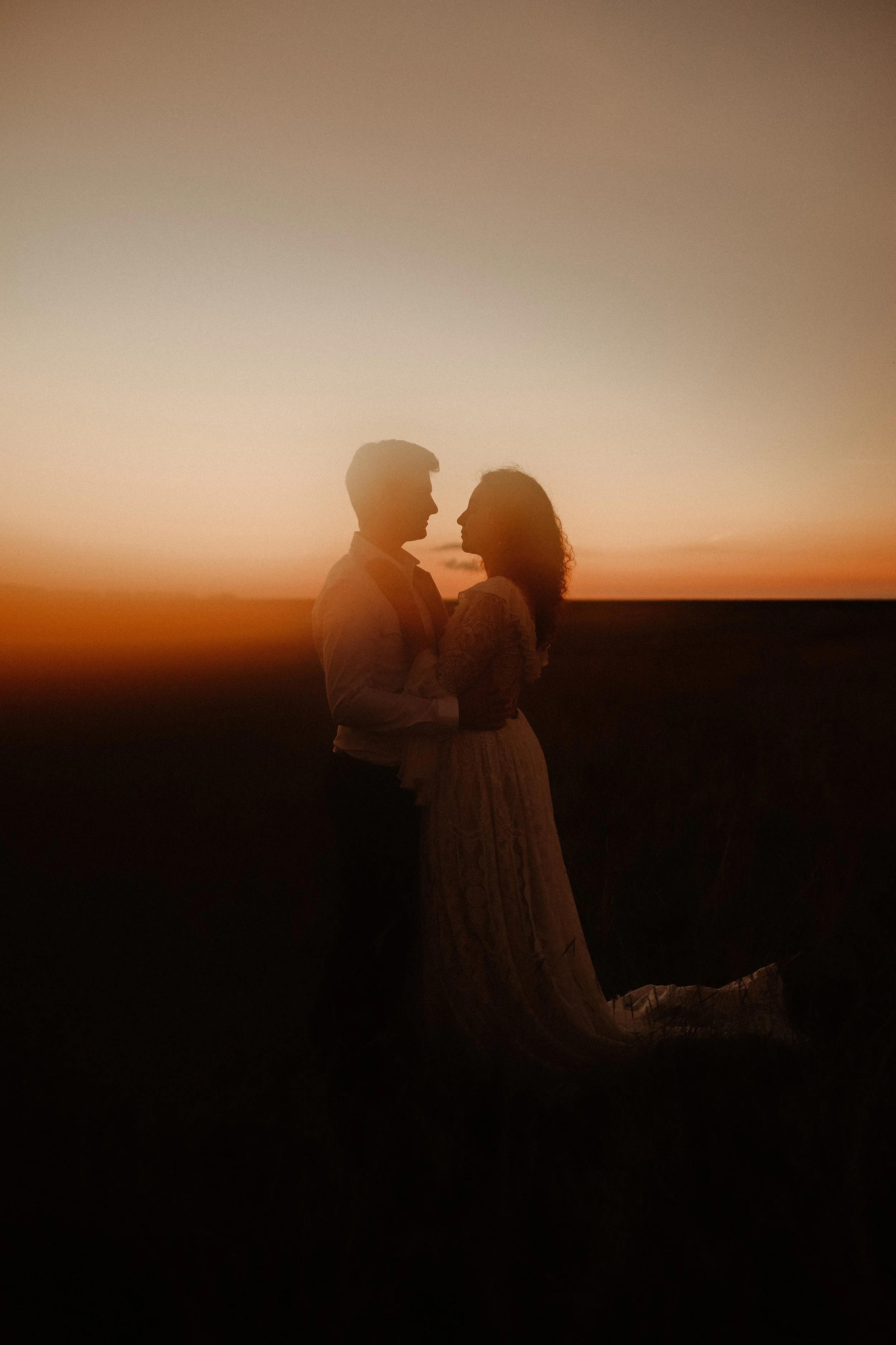 Silhouette d'un couple s'enlaçant lors d'un coucher de soleil, fond orange et ciel clair.