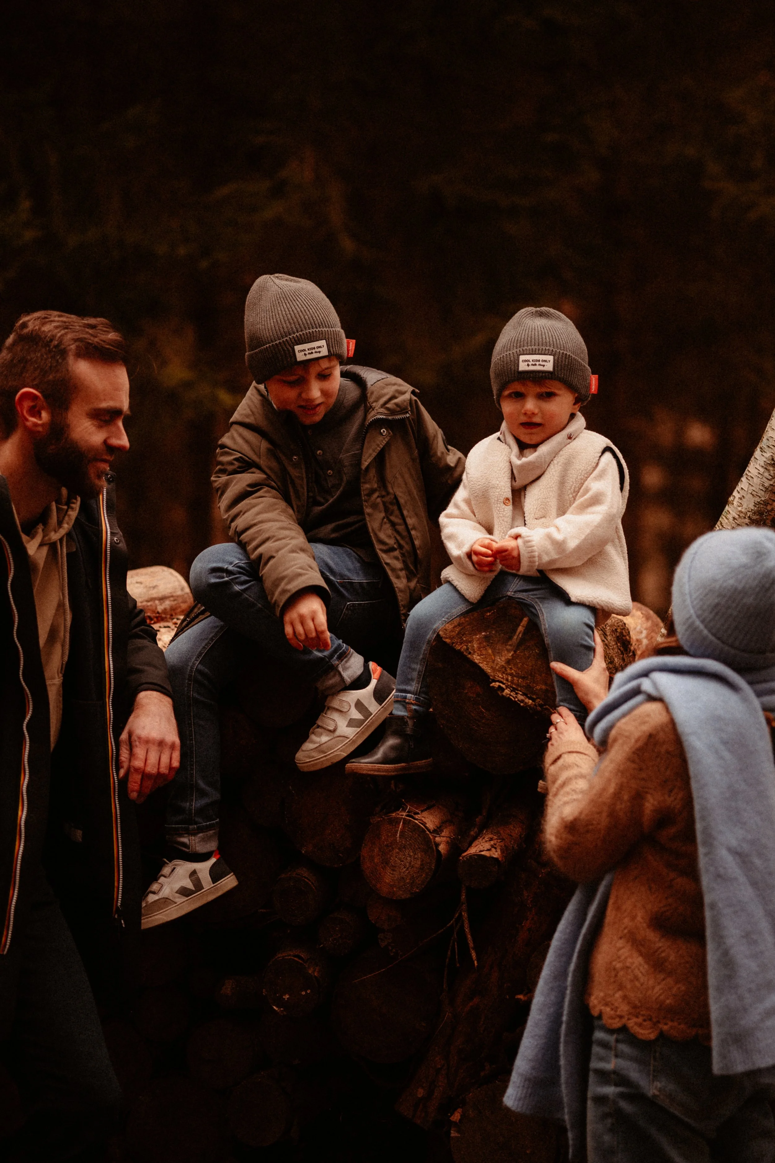 Groupe d'adultes et d'enfants discutant et passant du temps ensemble dans une forêt, parmi des troncs d'arbres.