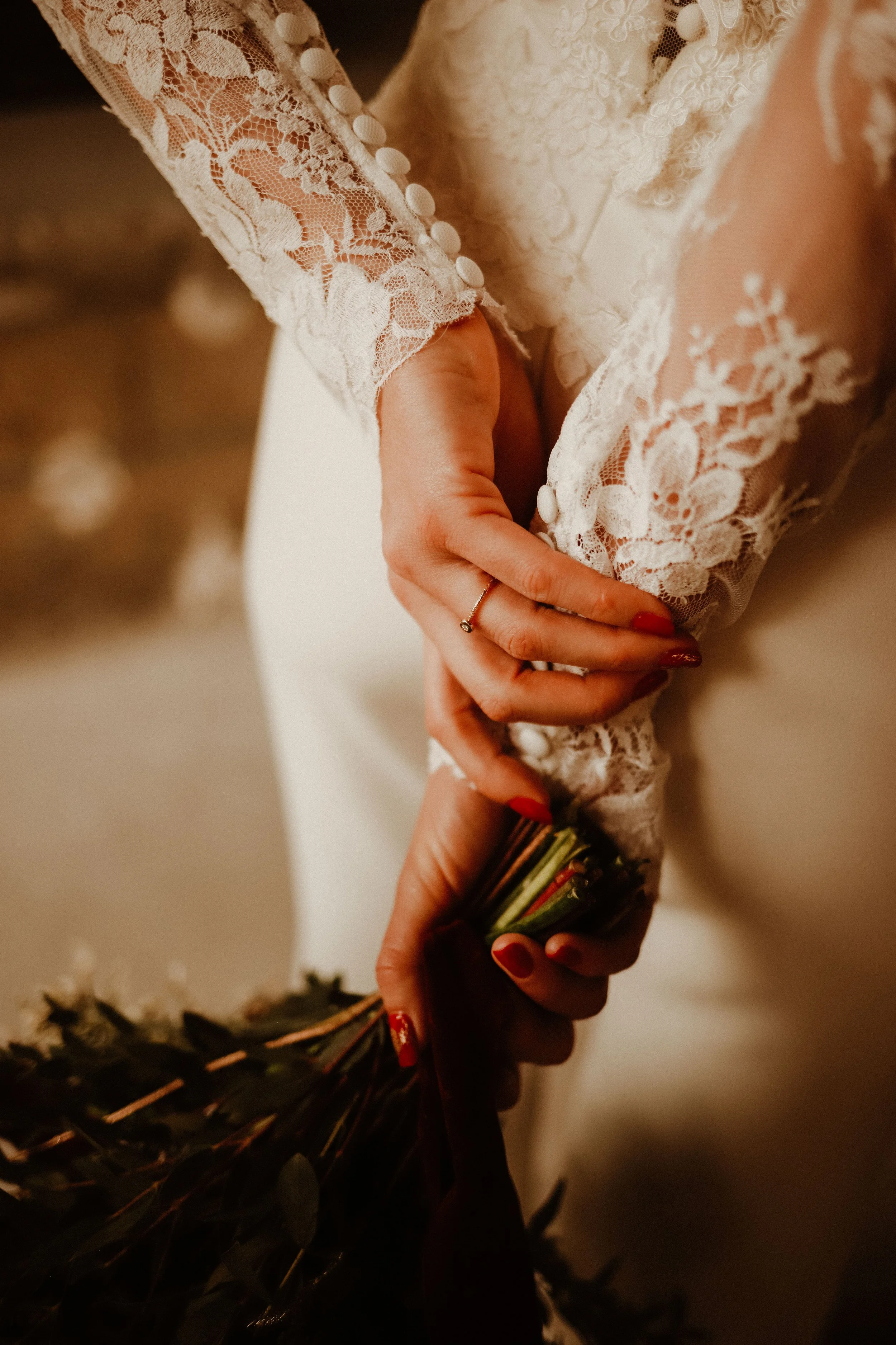 Détail d'une main tenant un bouquet de fleurs avec robe en dentelle blanche et boutons. Altération douce de la lumière et mise au point sur la main et la dentelle.