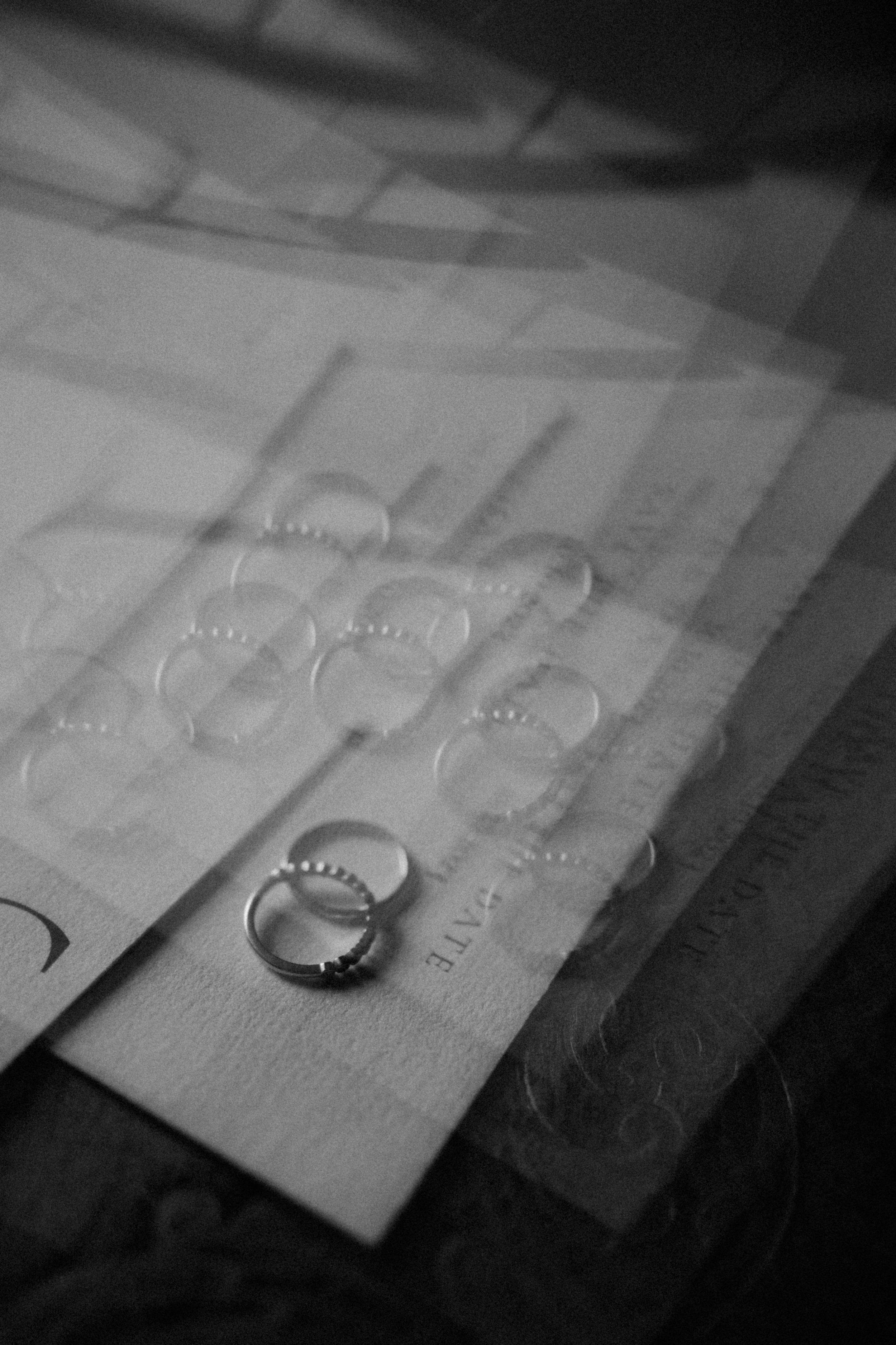 Des alliances en métal enroulées autour de petites cartouches ou capsules sur un fond de papier, en noir et blanc.