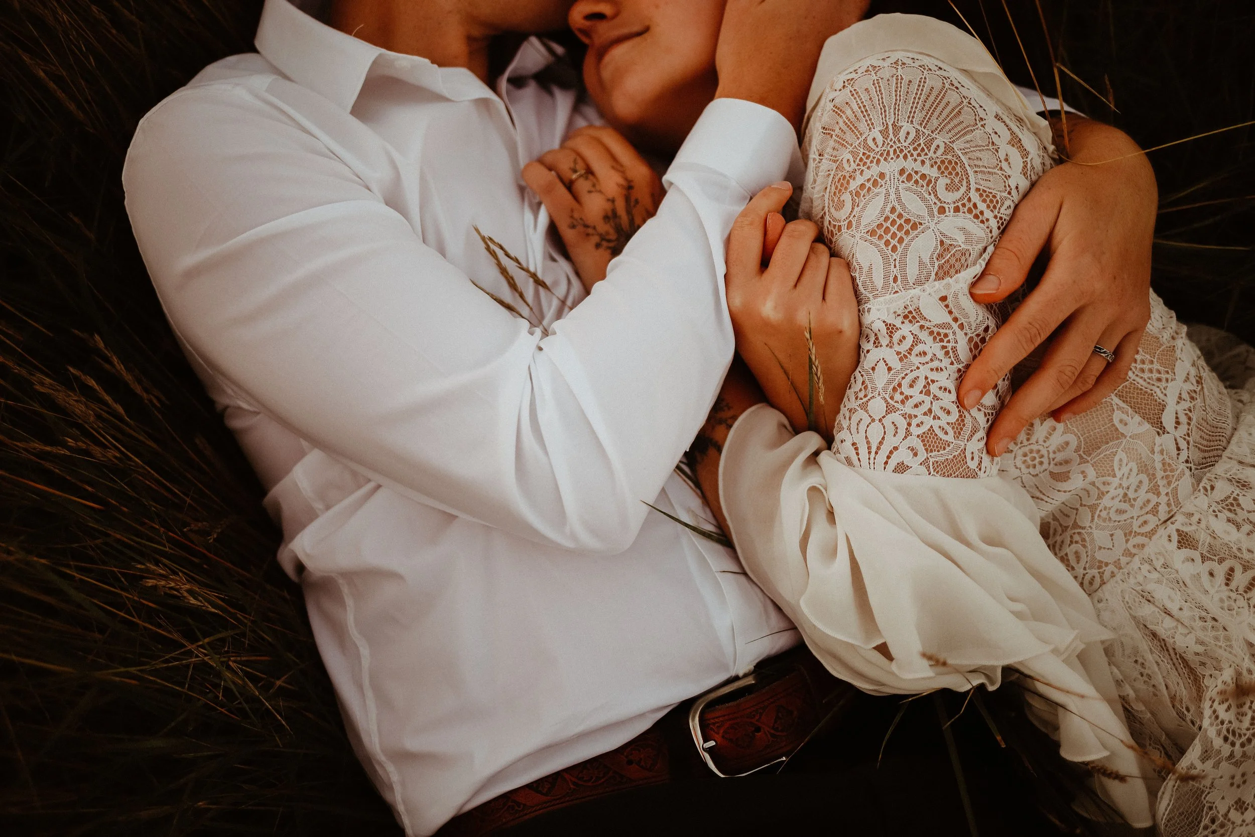 Un couple en vêtements blancs, elle en robe en dentelle, s'étreignent dans une nature naturelle, partageant un moment intime et tendre.