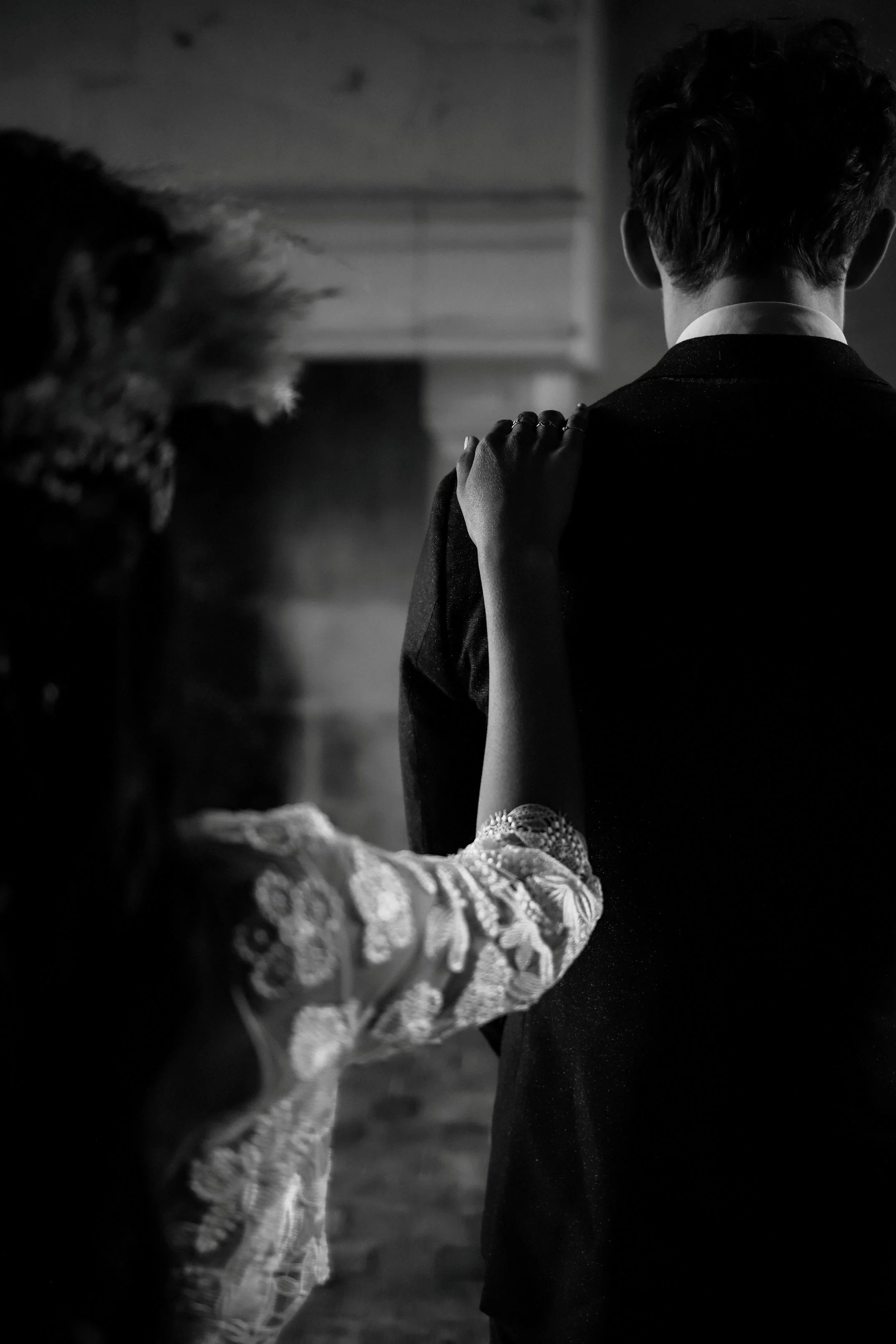 Une personne tient l'épaule d'un homme en costume lors d'une scène en noir et blanc.