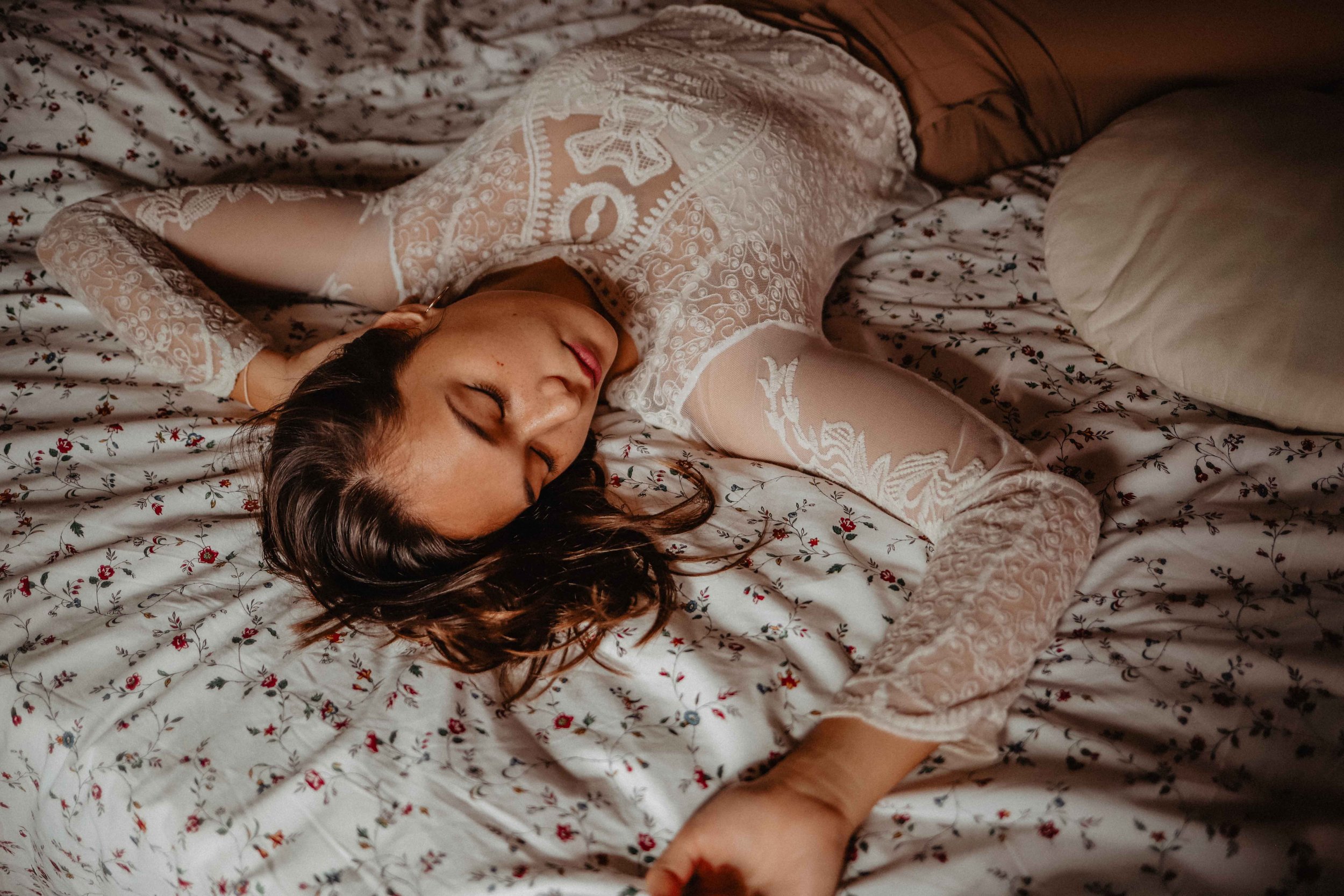 Femme allongée sur un lit, dormant, en vêtements en dentelle blanche, avec des draps à motif floral.