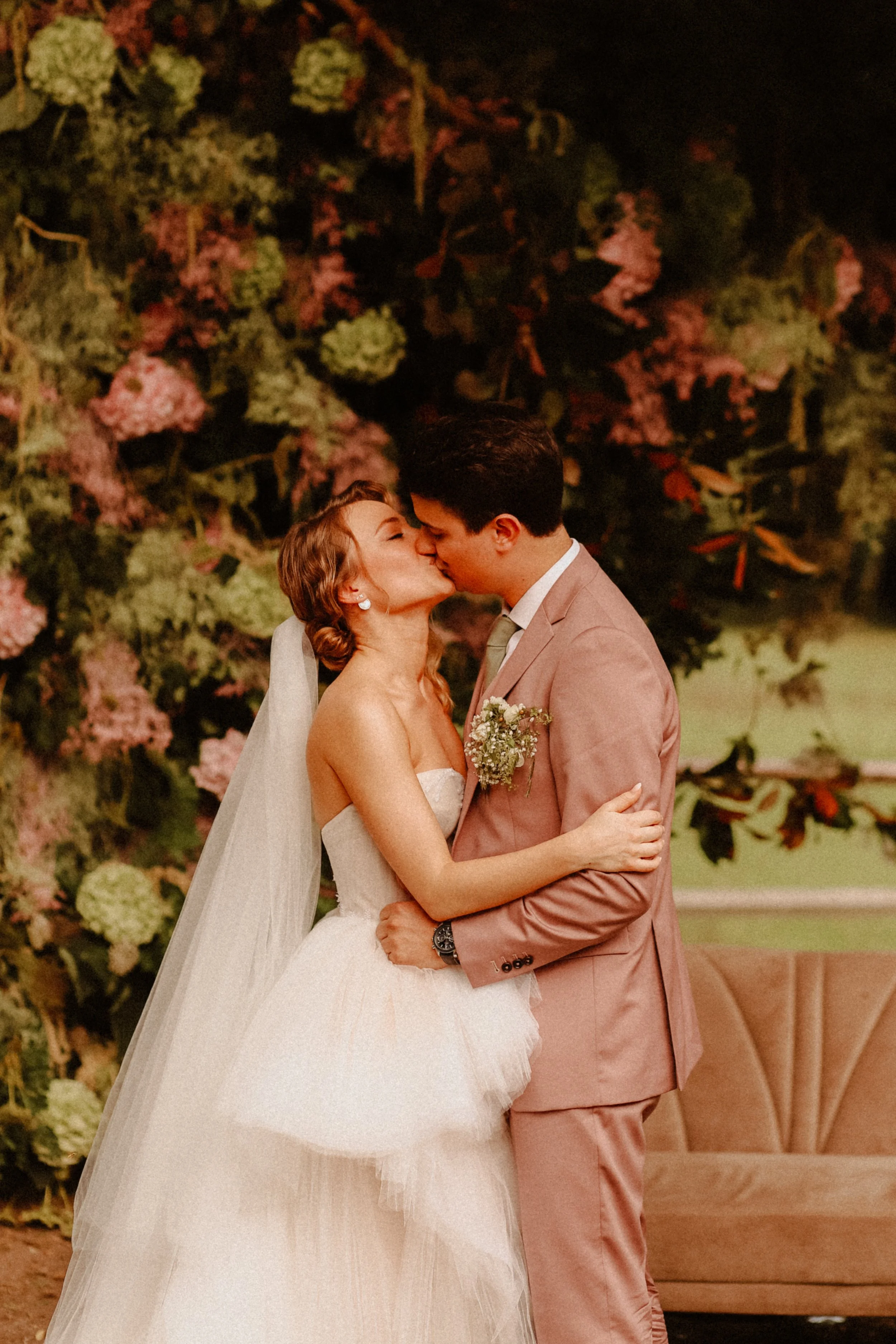 Un couple de mariés s'embrassant lors de leur mariage, avec un décor floral en arrière-plan.
