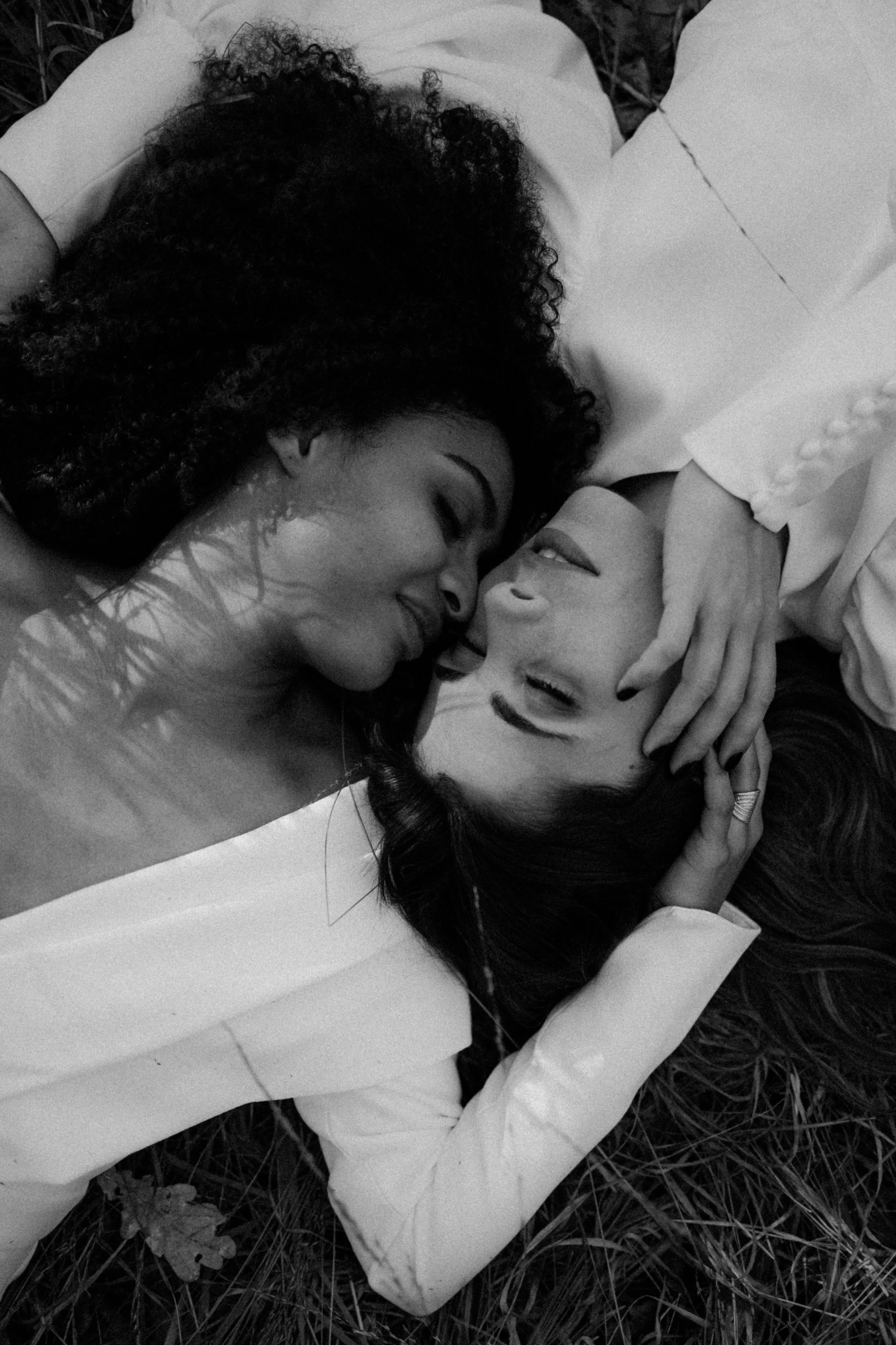 Deux femmes allongées face à face sur l'herbe, se regardant tendrement avec leurs yeux fermés, partagent un moment intime.