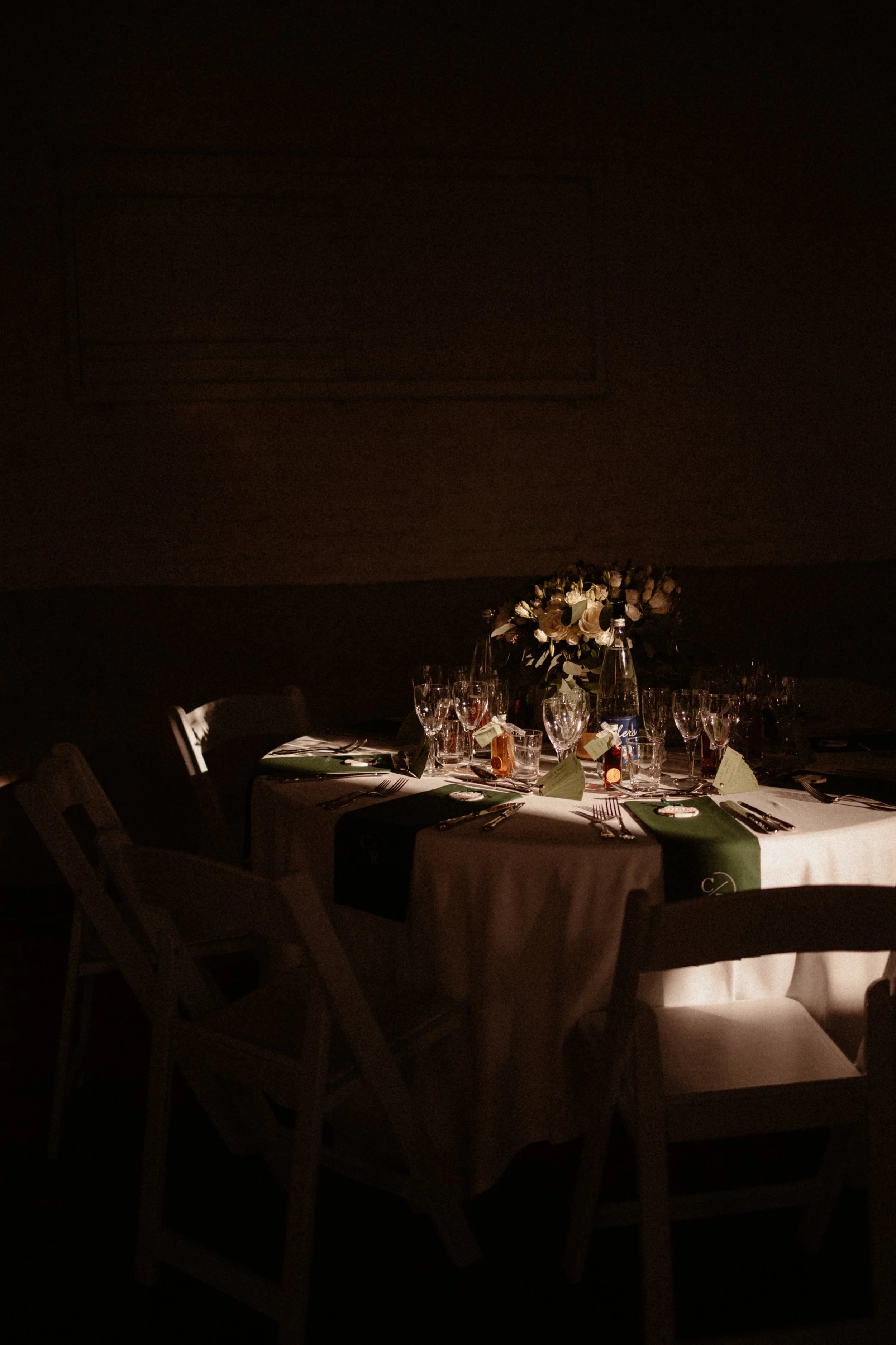 Table de fête élégante avec vaisselle, verres, flacons, et une grande composition florale, dans une ambiance sombre et chaleureuse.