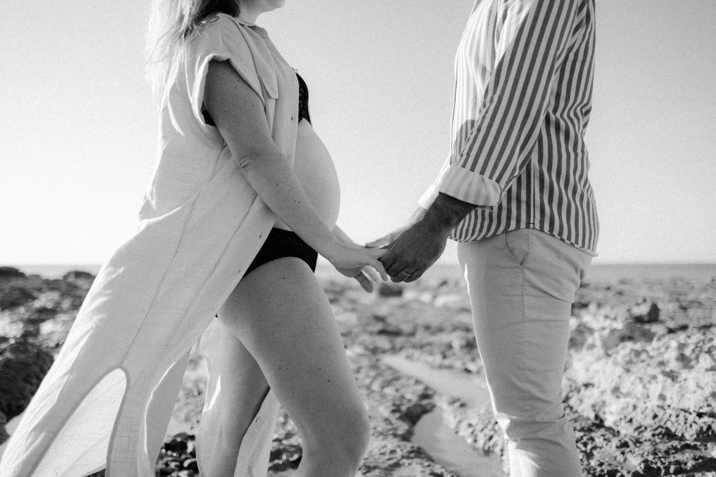 Un couple tenant la main sur la plage, en noir et blanc.