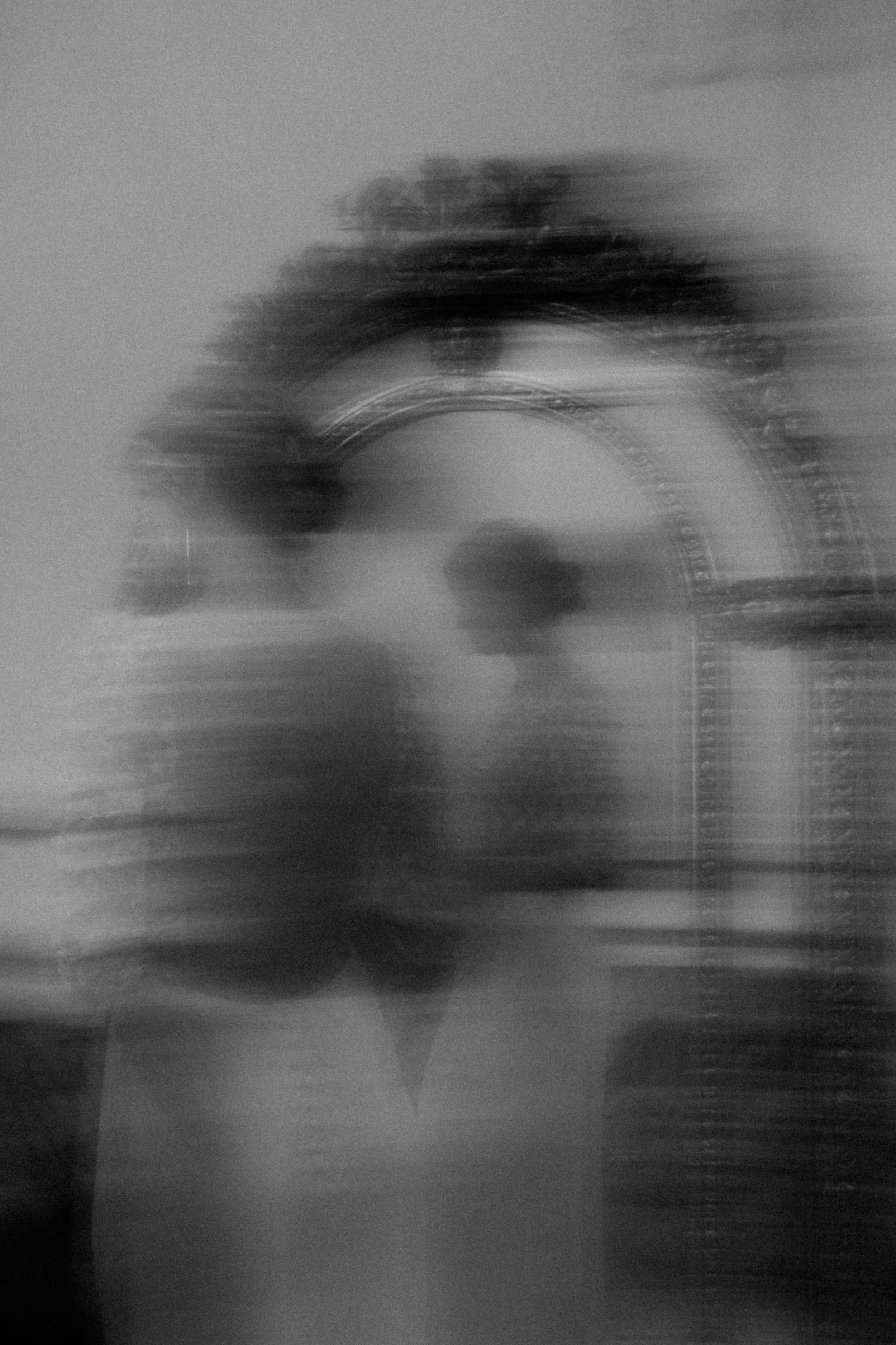 Photo floue en noir et blanc d'un visage avec un sautoir ou collier autour du cou, miroir ancien en arrière-plan.