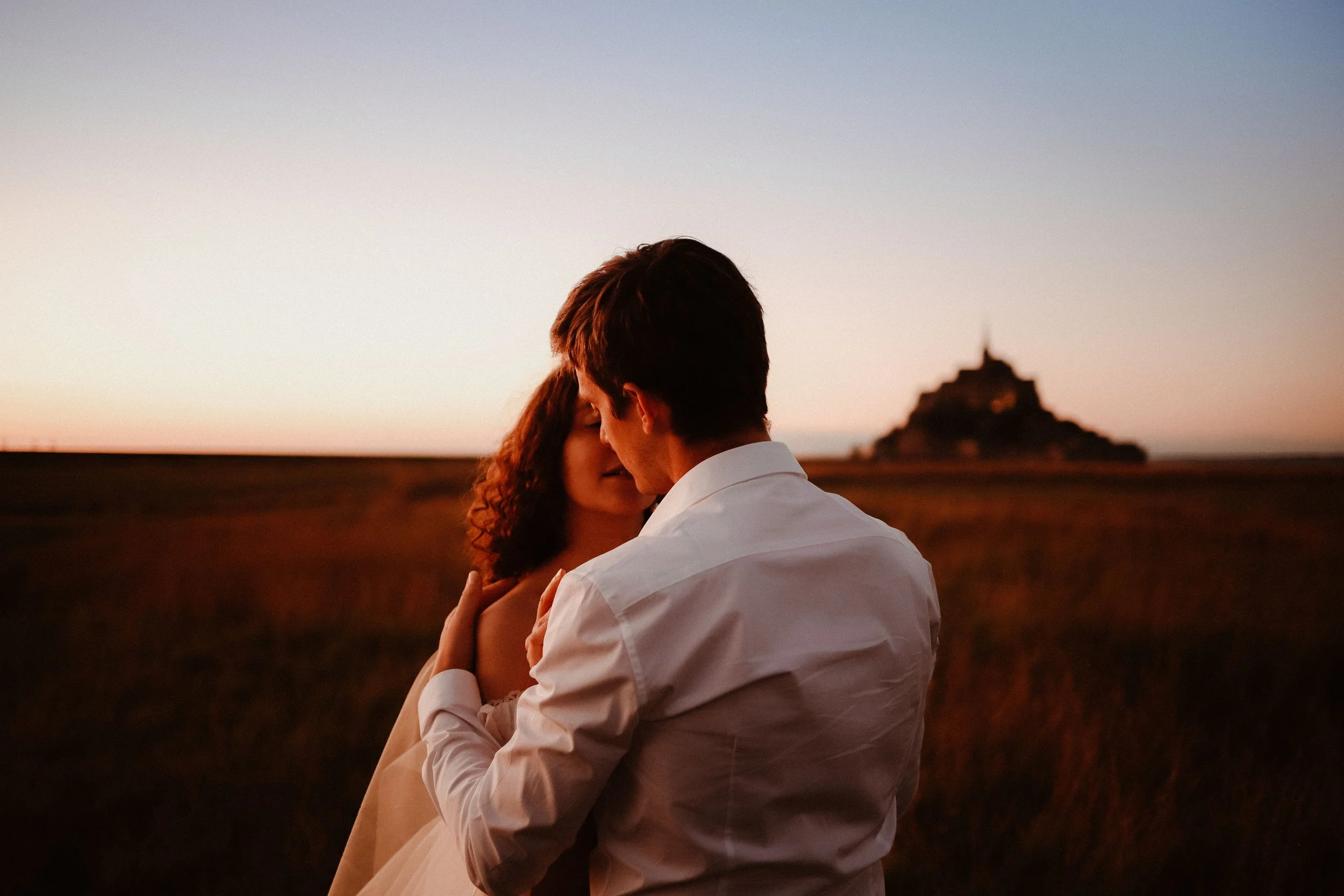 Un couple s'embrassant tendrement lors d'un coucher de soleil, avec une silhouette d'une montagne en arrière-plan.