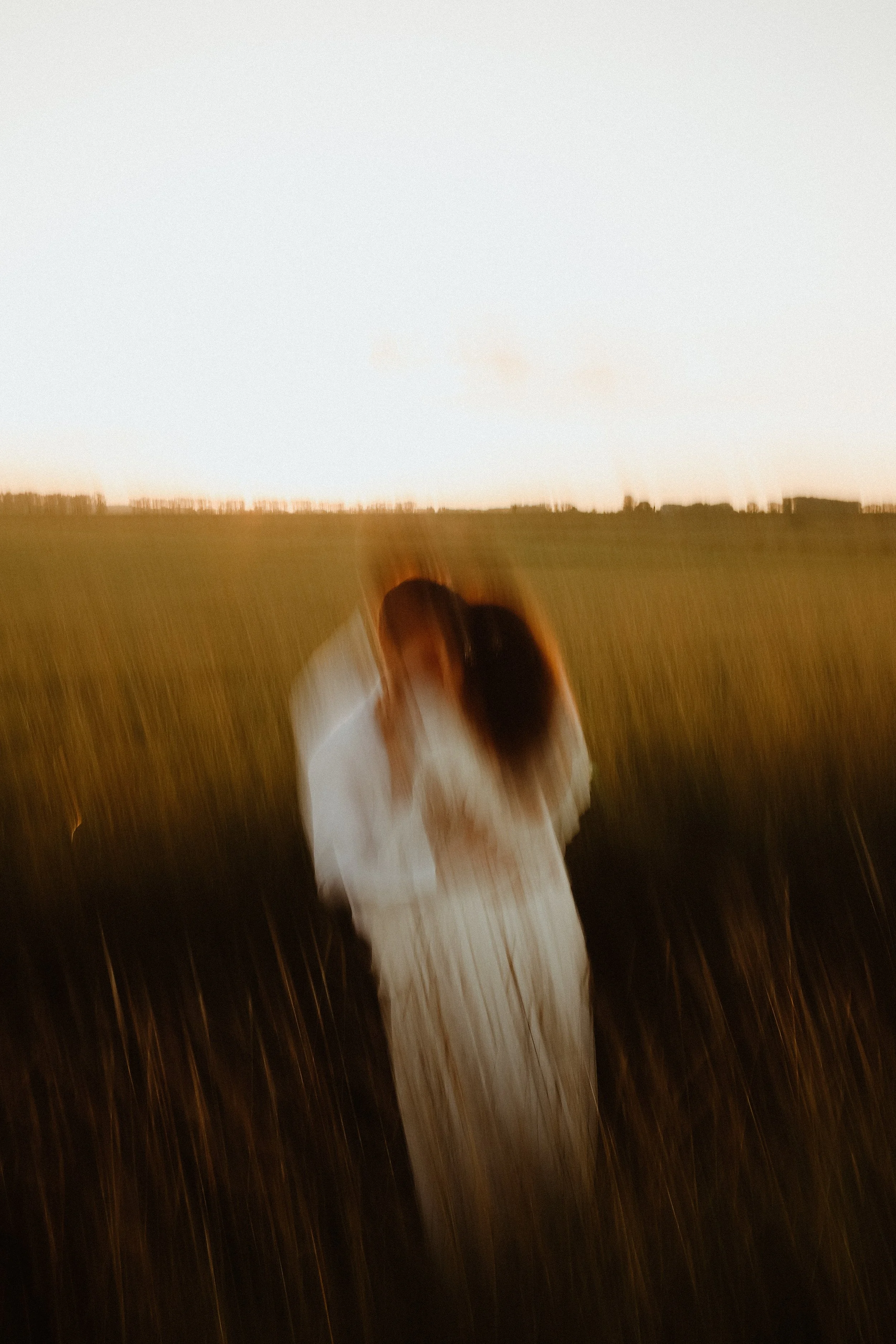 Une femme en robe blanche dans un champ lors du coucher du soleil, photo floue avec mouvement.
