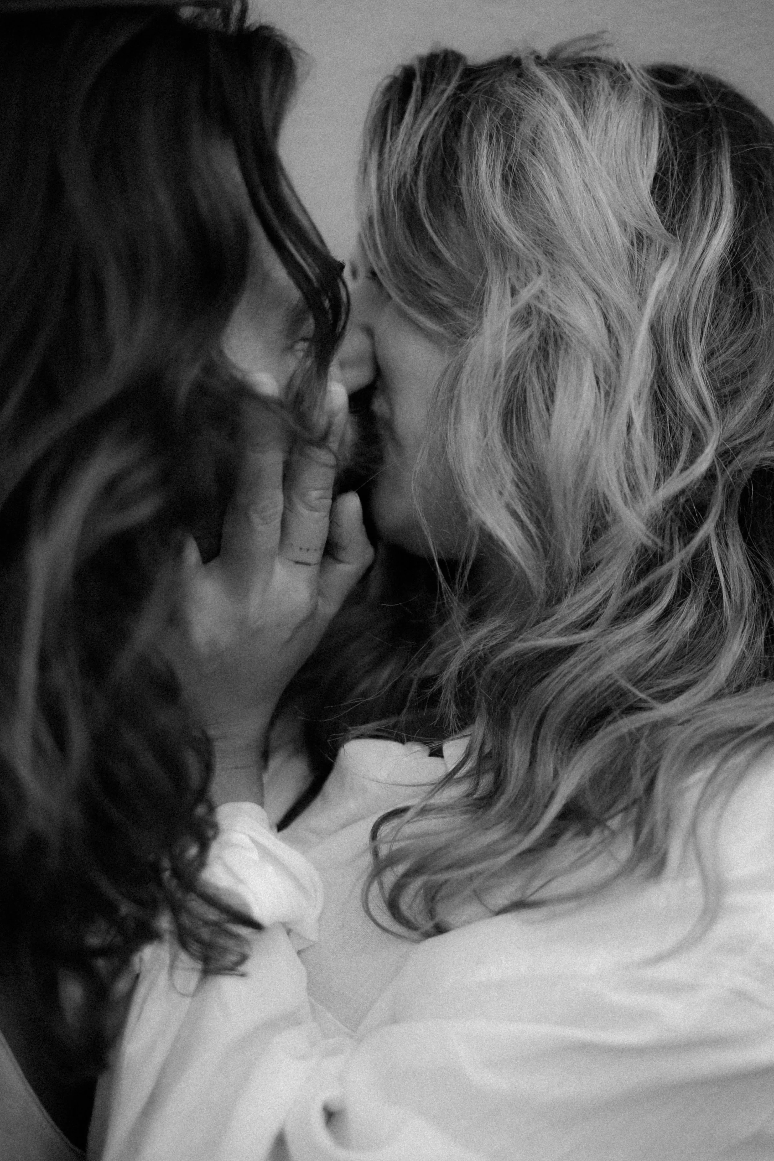 Deux femmes s'embrassent tendrement, l'une avec des cheveux bouclés blonds et l'autre avec des cheveux longs foncés, dans un noir et blanc intime.