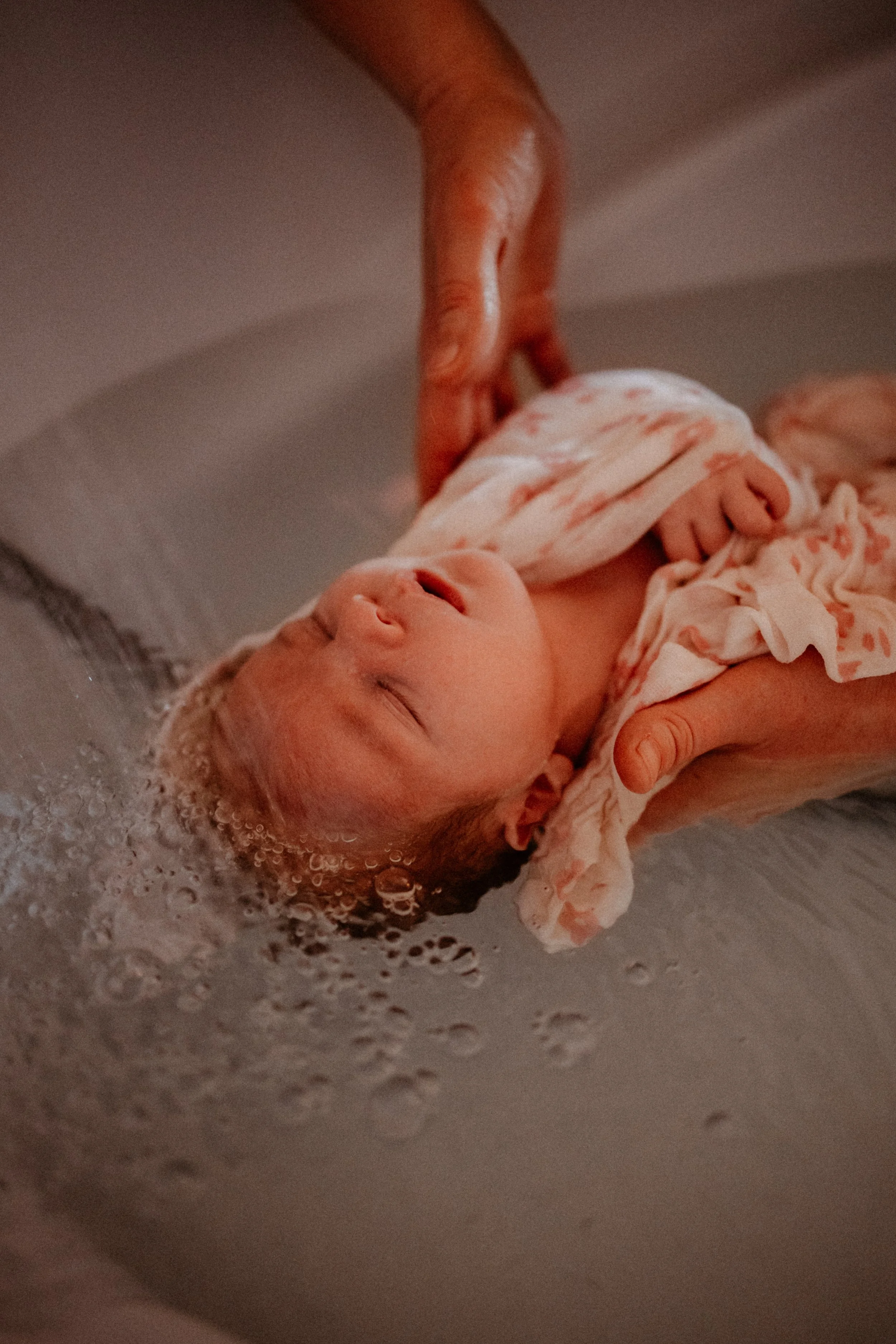 Un bébé en train d'être baigné dans une bassine, une personne l'aide à se laver.