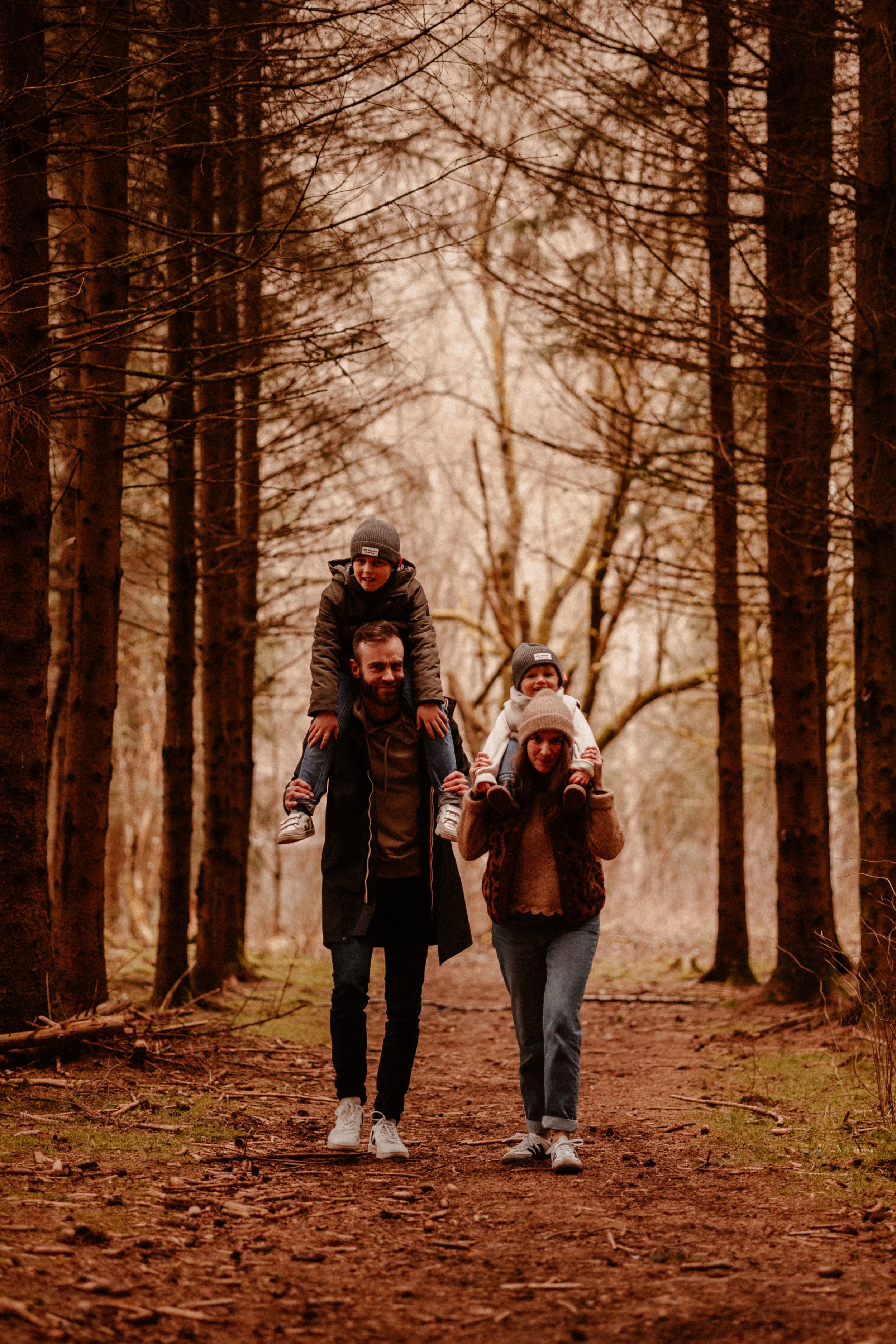 Une famille marche dans une forêt en automne, deux adultes portant deux enfants sur leurs épaules.