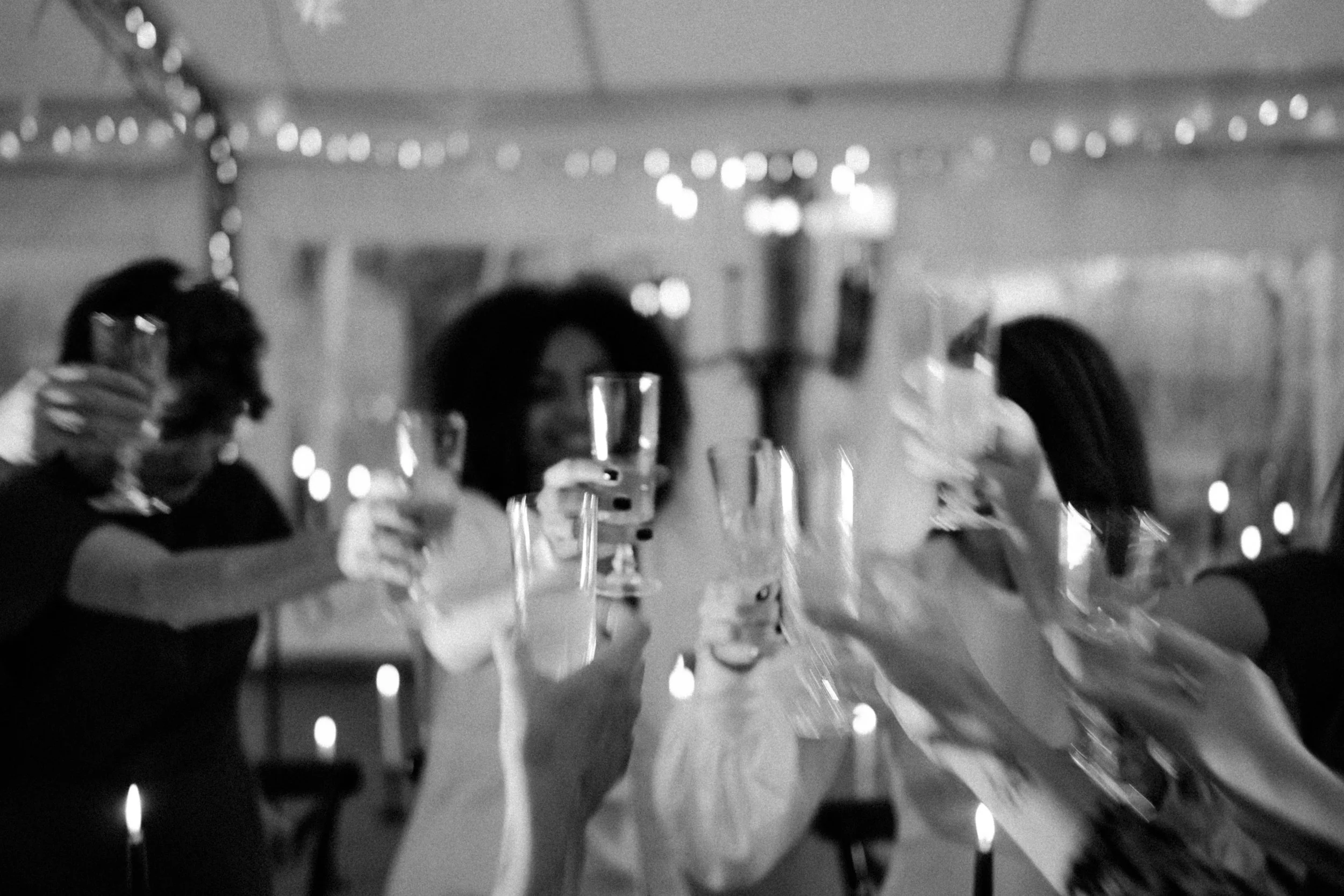 Groupe de personnes célébrant une fête, portant des verres à toast, dans une ambiance festive avec des lumières et bougies.