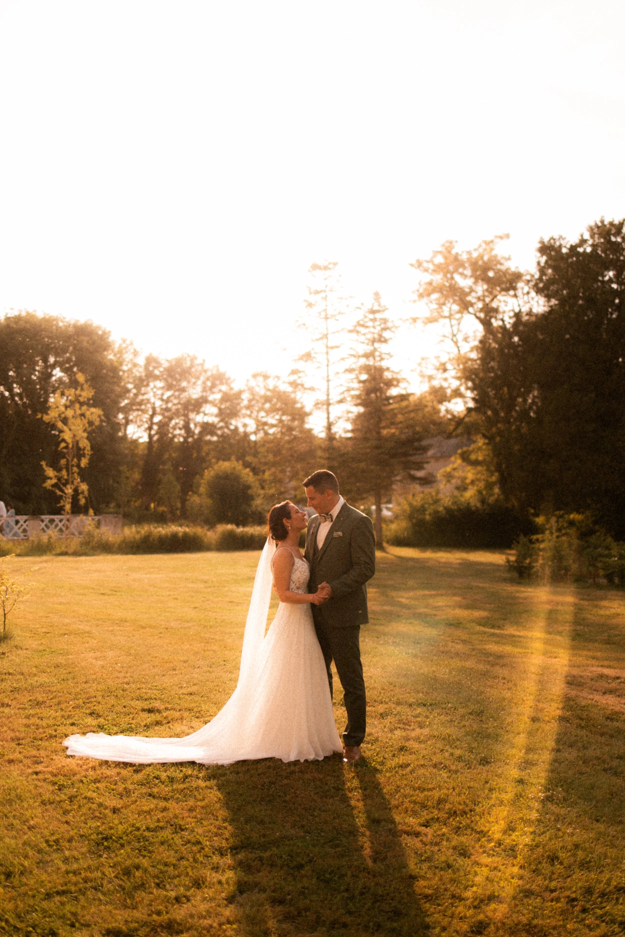 Un couple de mariés danse dans un jardin au coucher du soleil.