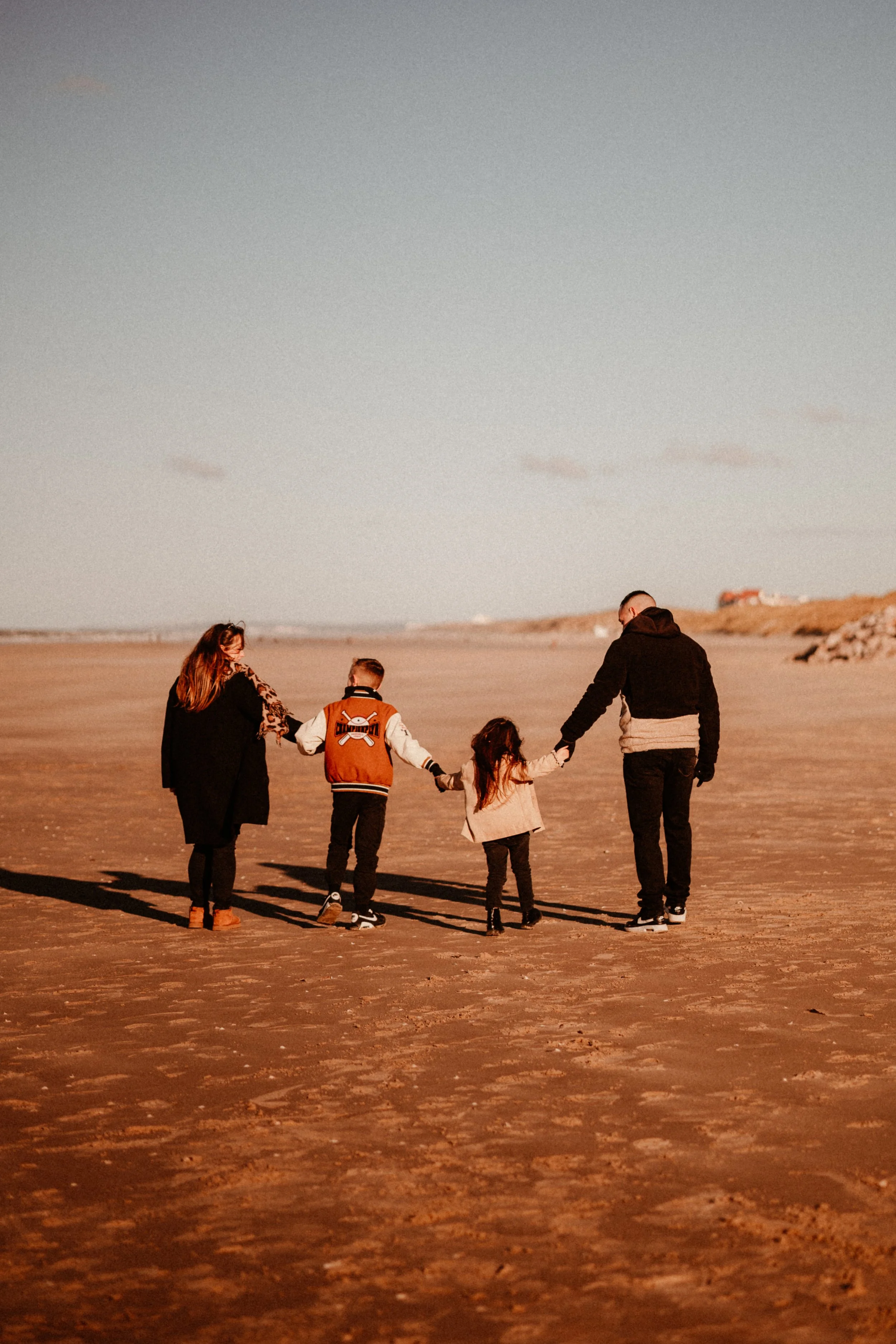 Une famille de quatre personnes marche sur une plage au coucher du soleil, tenant la main les uns des autres.