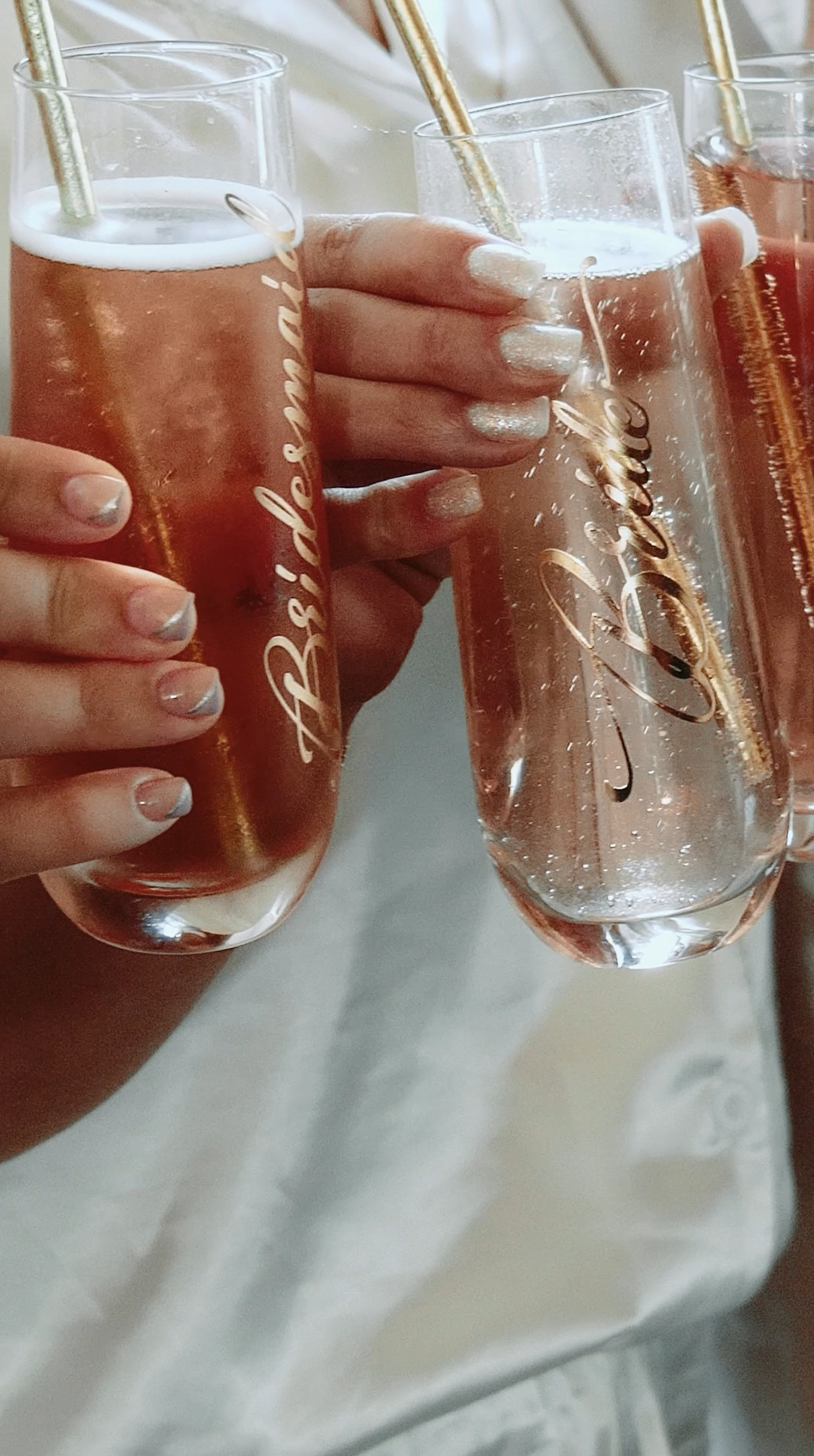 Multiple glasses of rosé champagne being clinked together in celebration, with people wearing white clothing in the background.